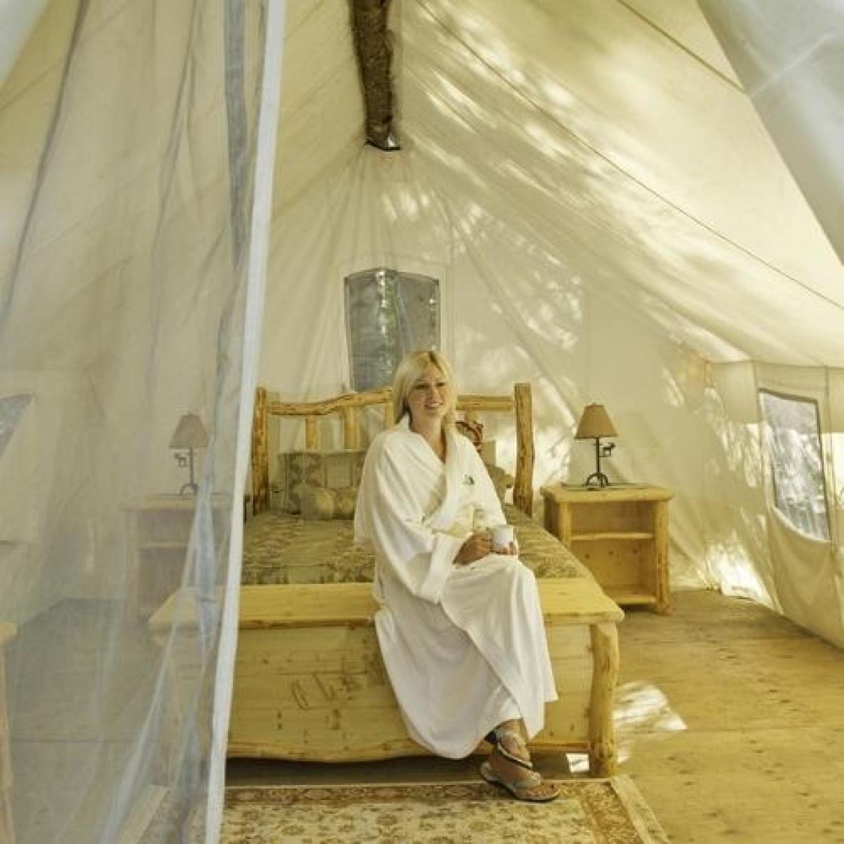 A person sitting on a bed in a glamping tent