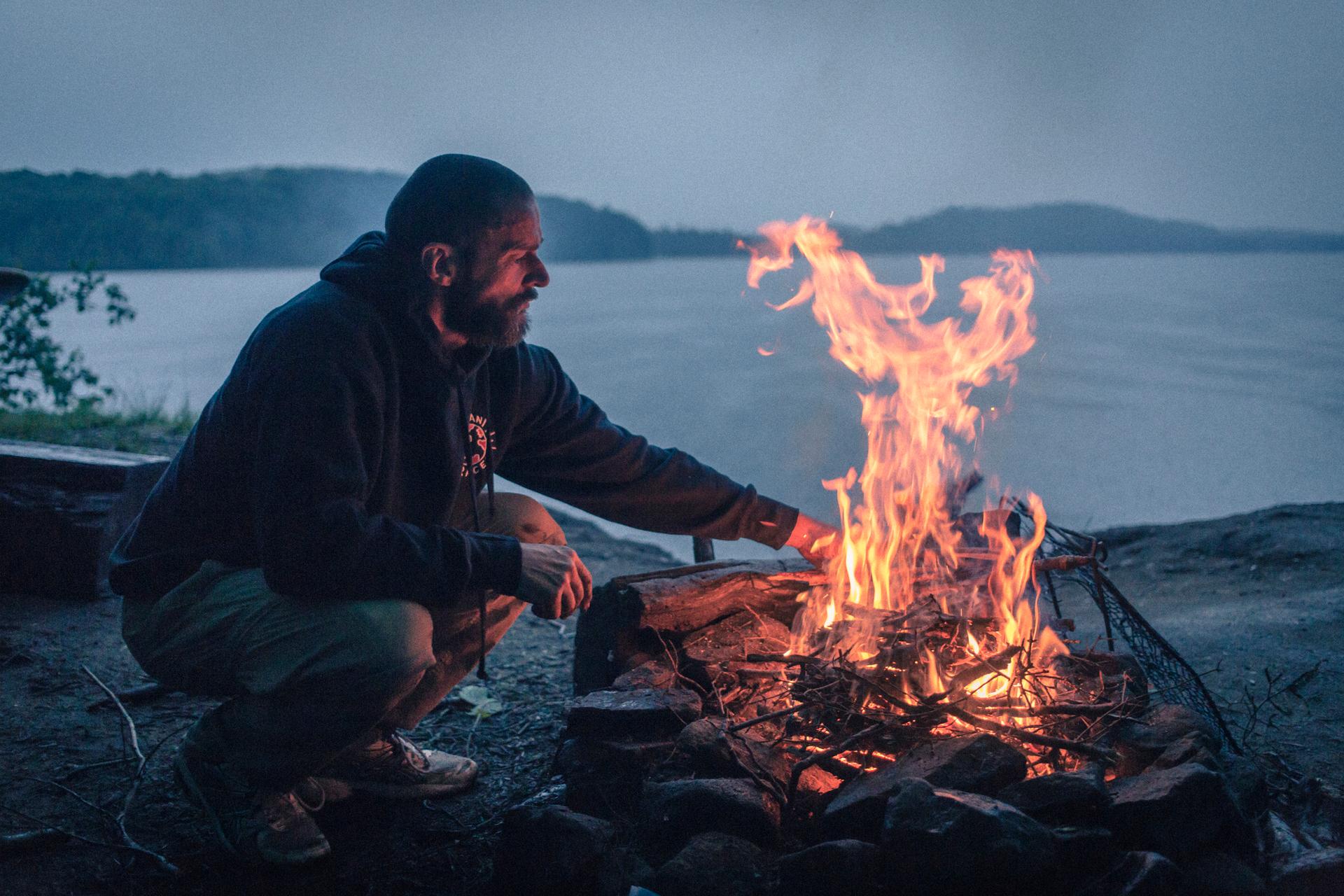 Fred Siriex squats next to a blazing outdoor fire