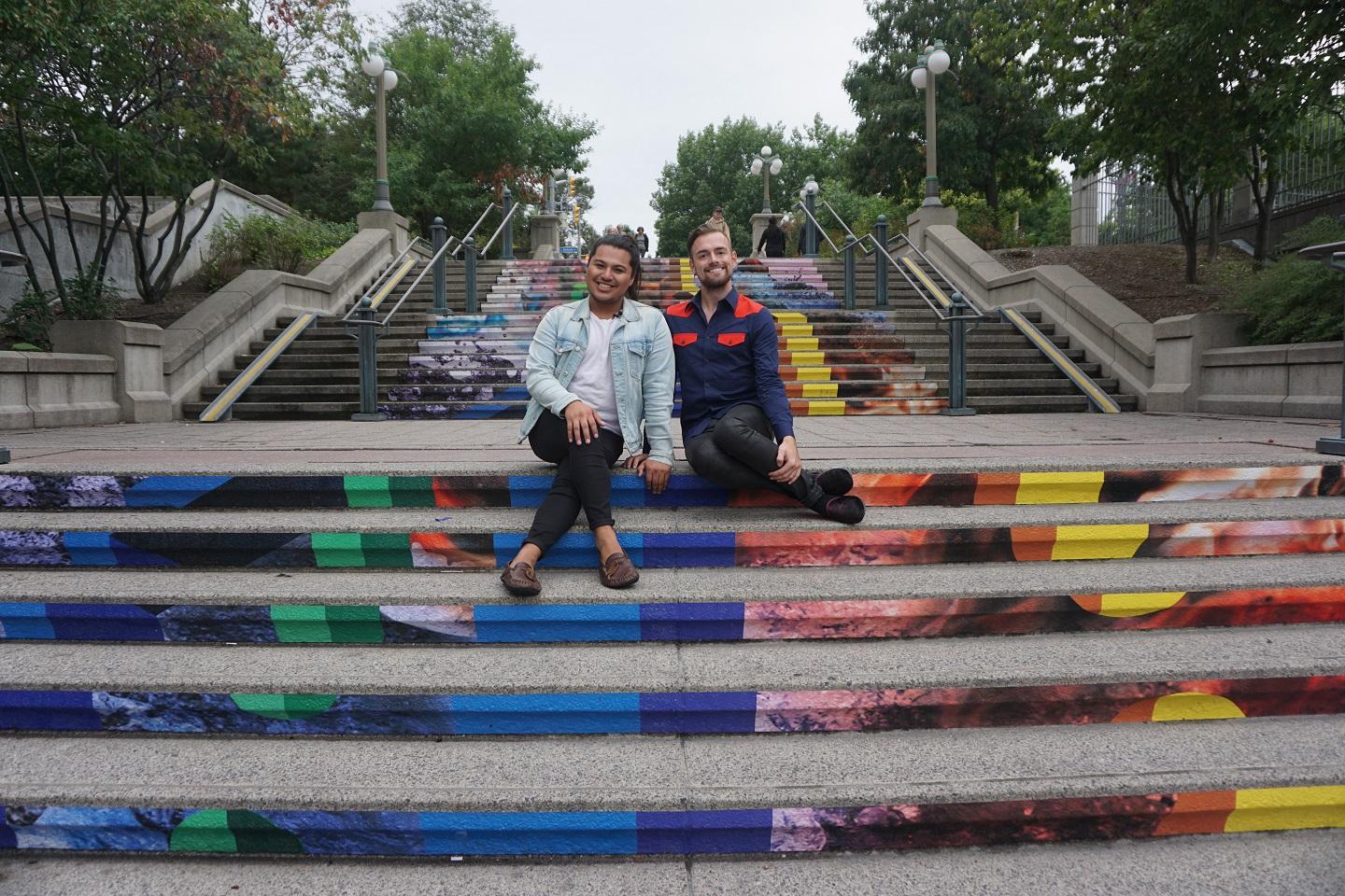 A couple, Brett and Cameron, sit together on some pride-painted steps in Ottawa