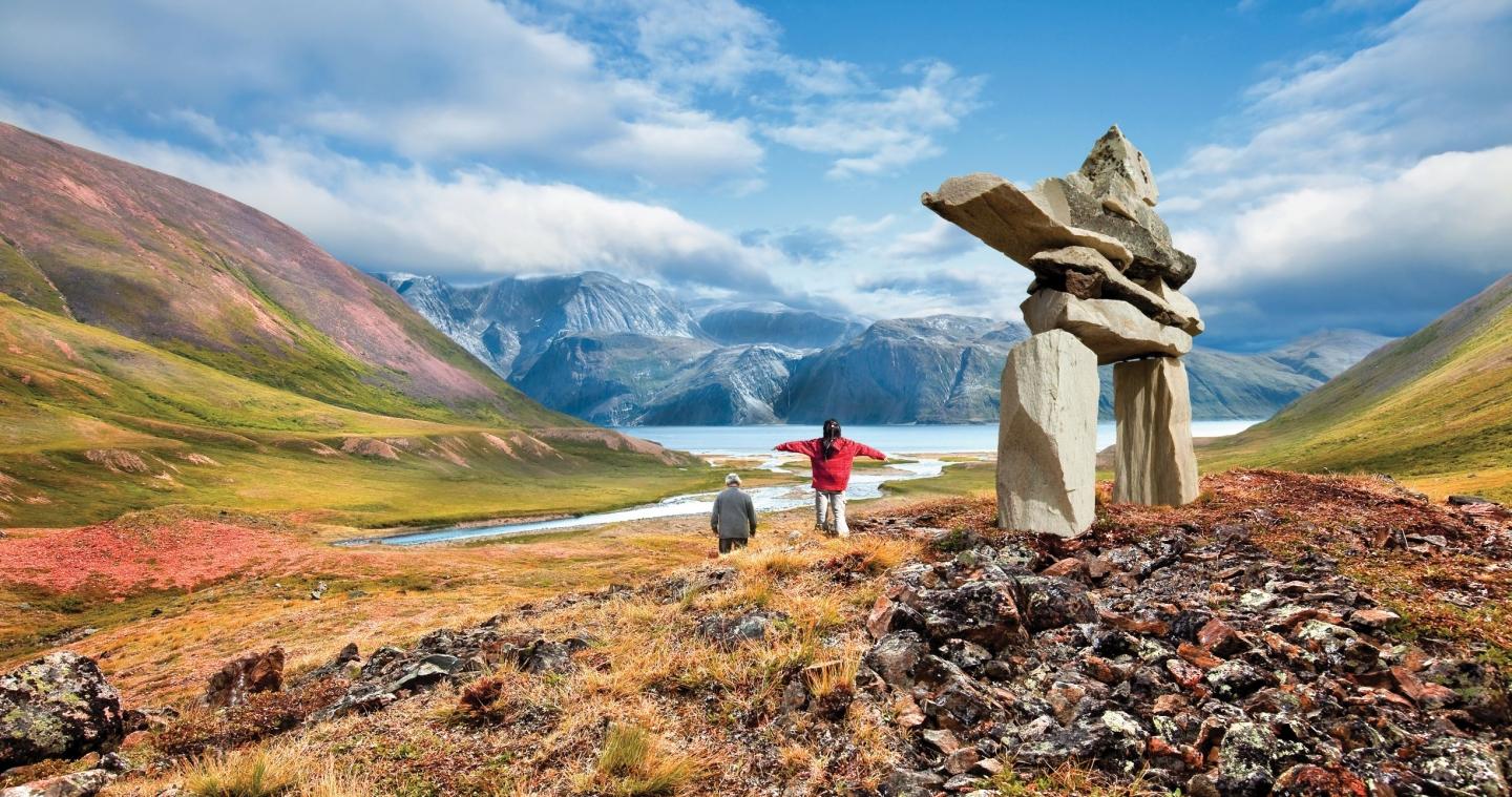 Two travellers walk alongside an inukshuk in the Torngat mountains