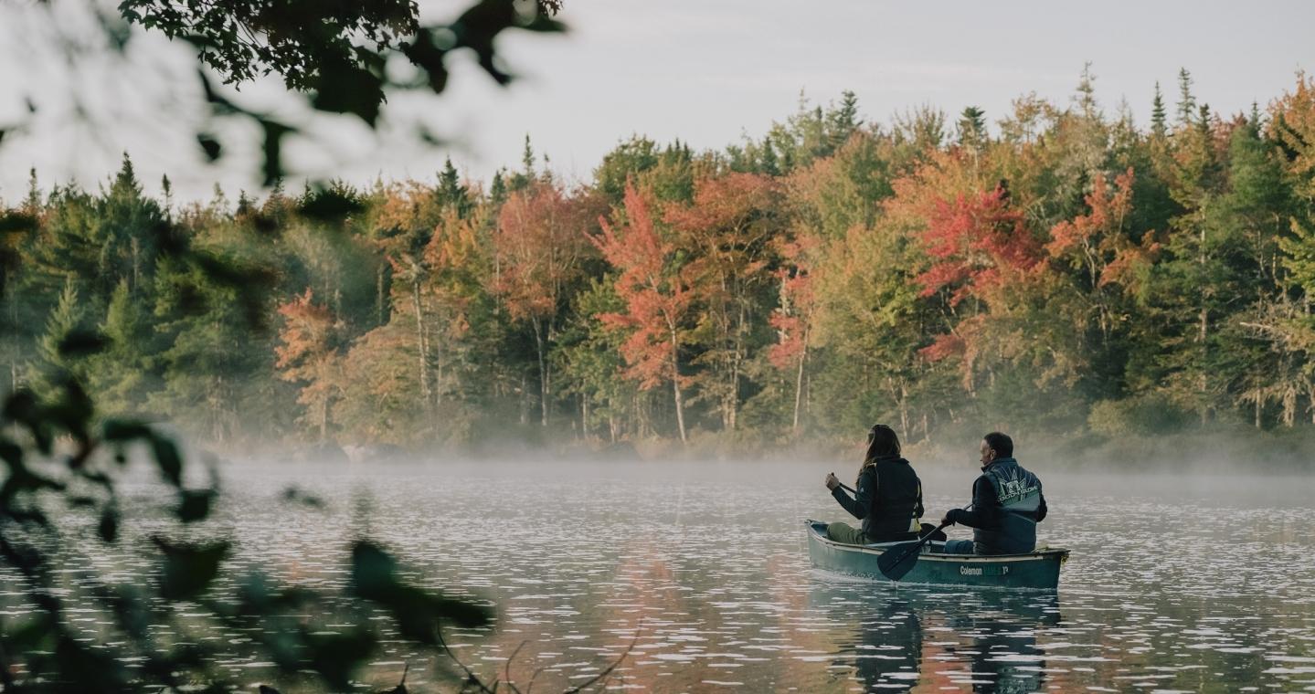 Two canoe paddlers explore a forest river in the fall