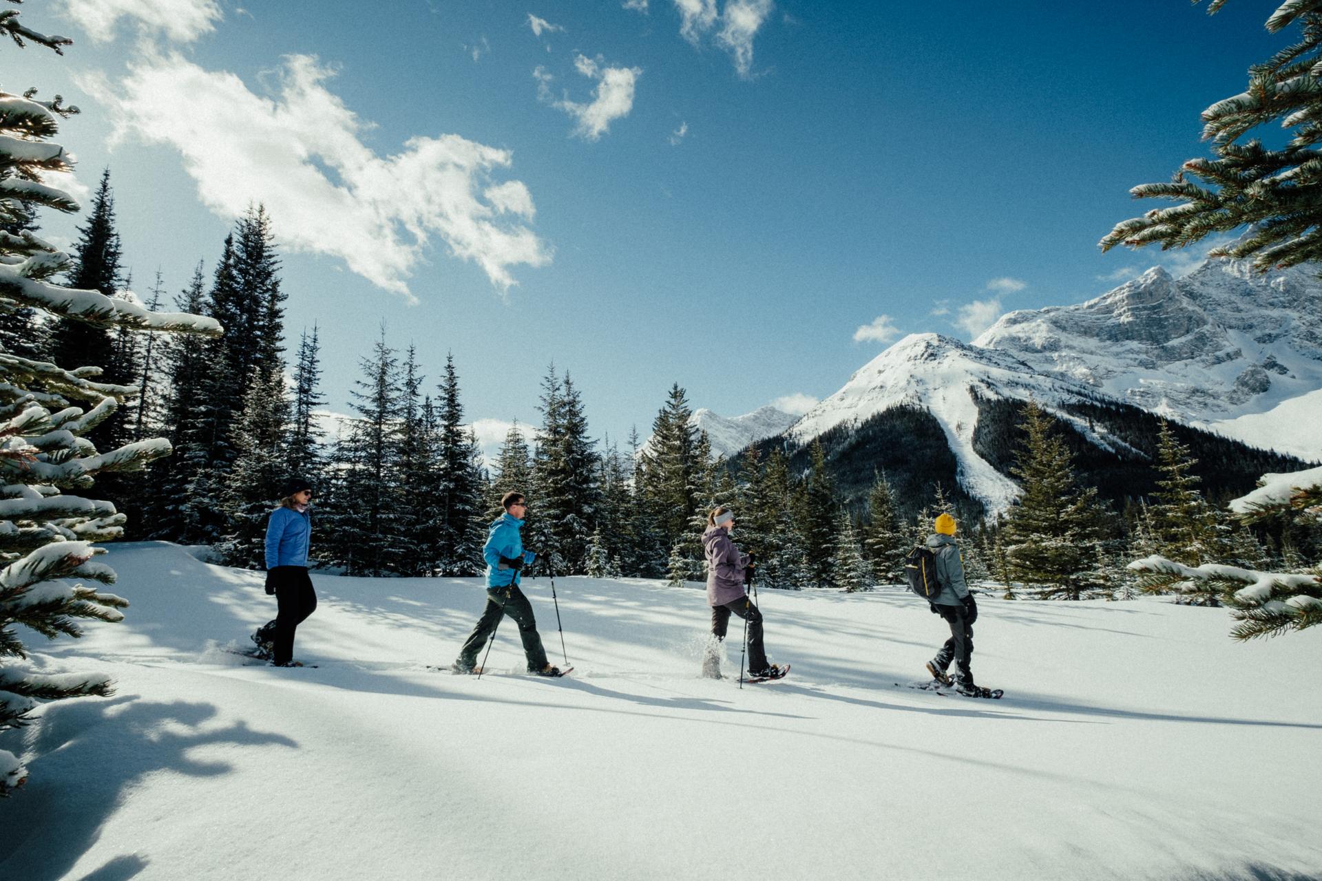 Four people snowshoeing by snow-covered mountains in Canmore, AB