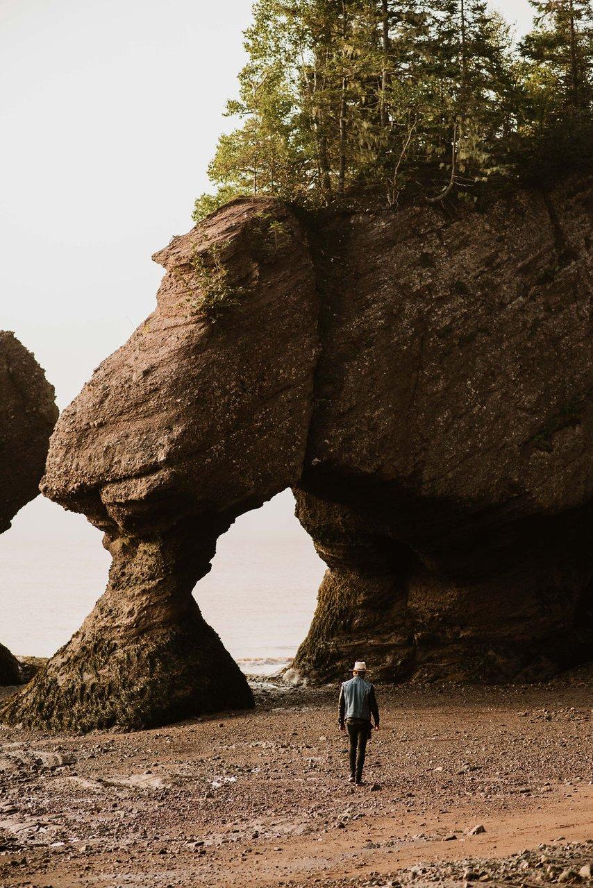 person walks in distance toward the Hopewell rocks, rocks high above that are carved out by risig tides