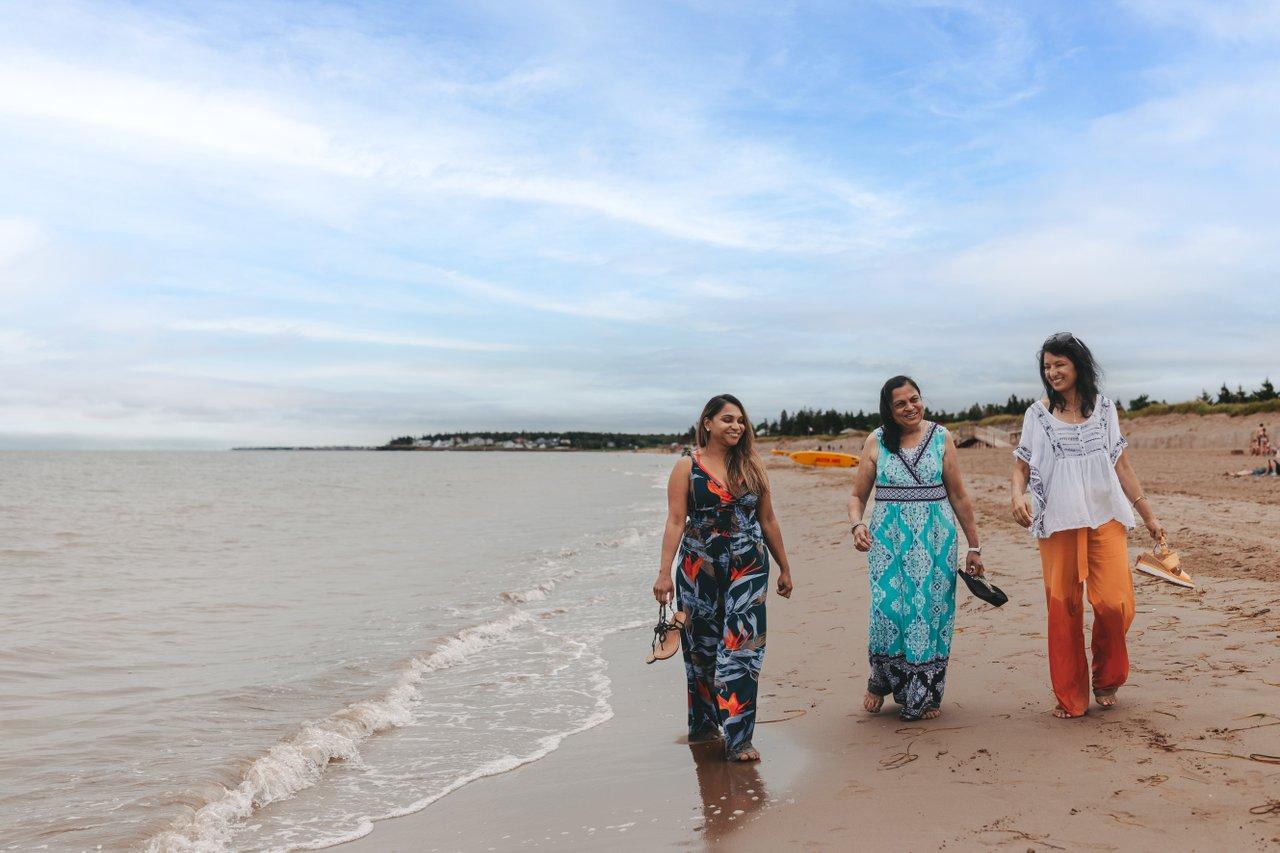 3 people walk along waterside of a beach