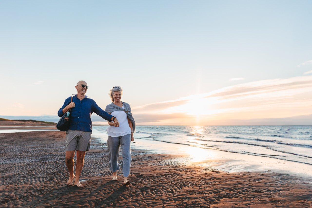 older couple walks along beach water at sunset