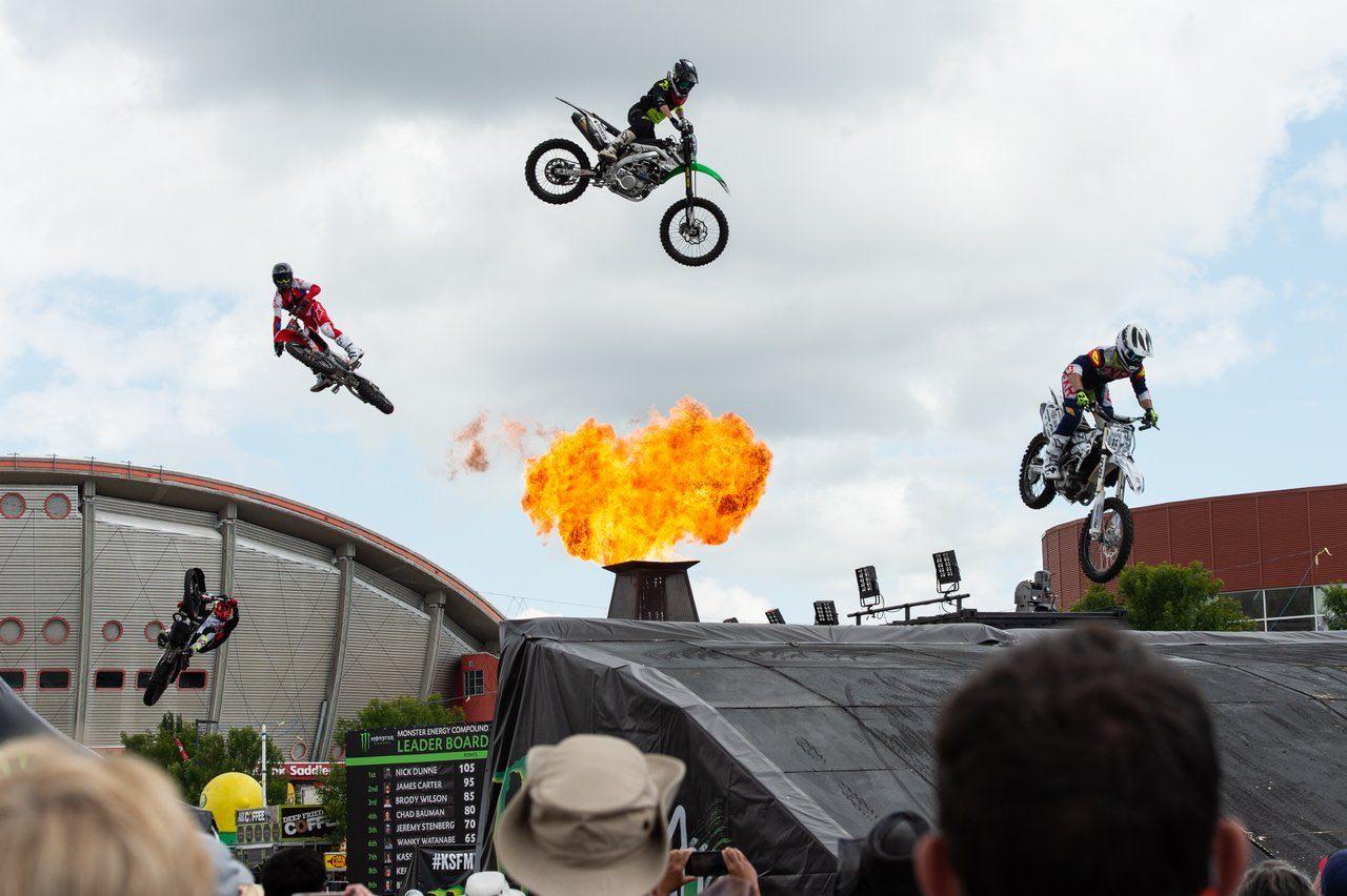 Four motocross racers jumping their bikes with flames in the background