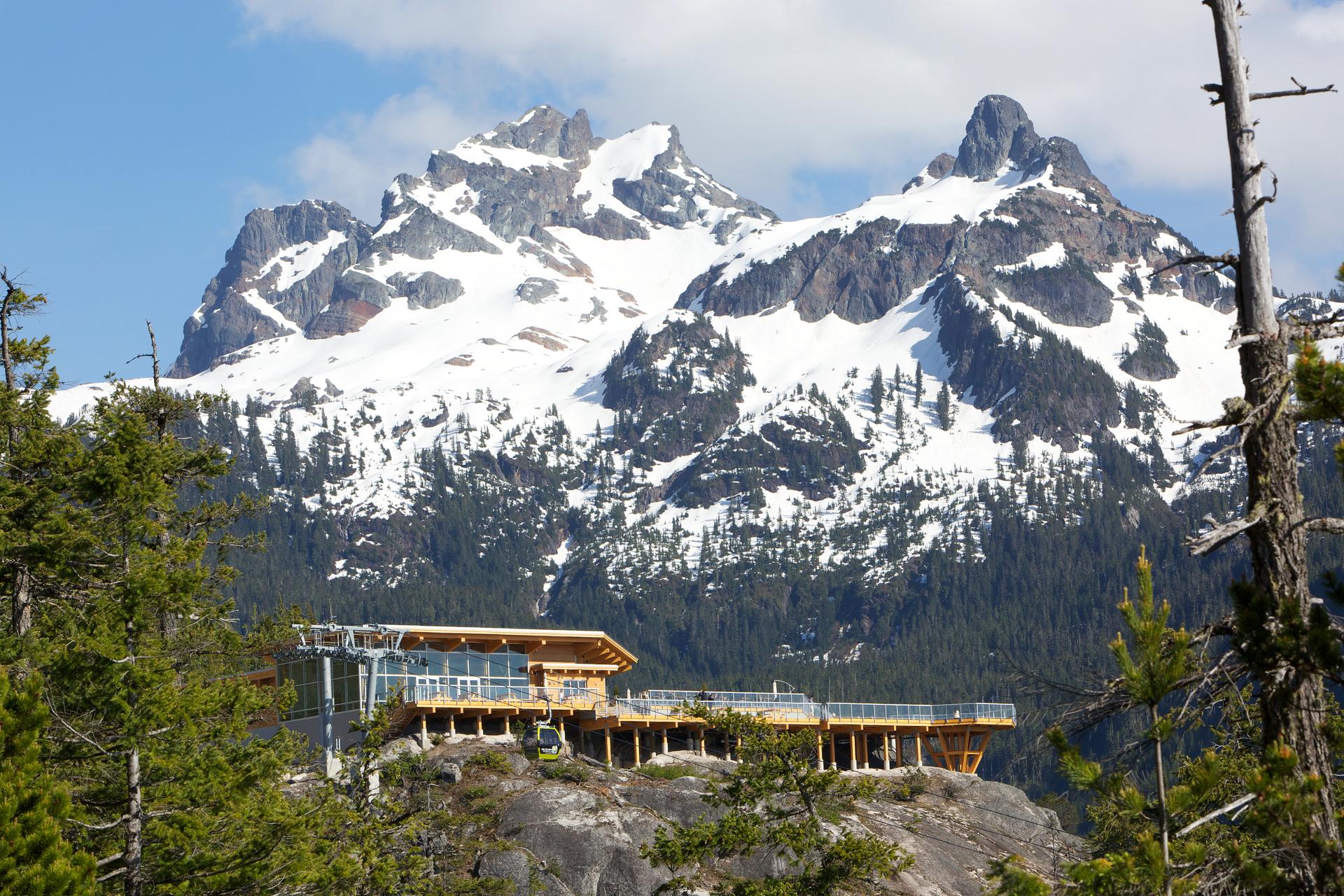 A building perched on a rocky ledge, with snow-covered mountains in the background.