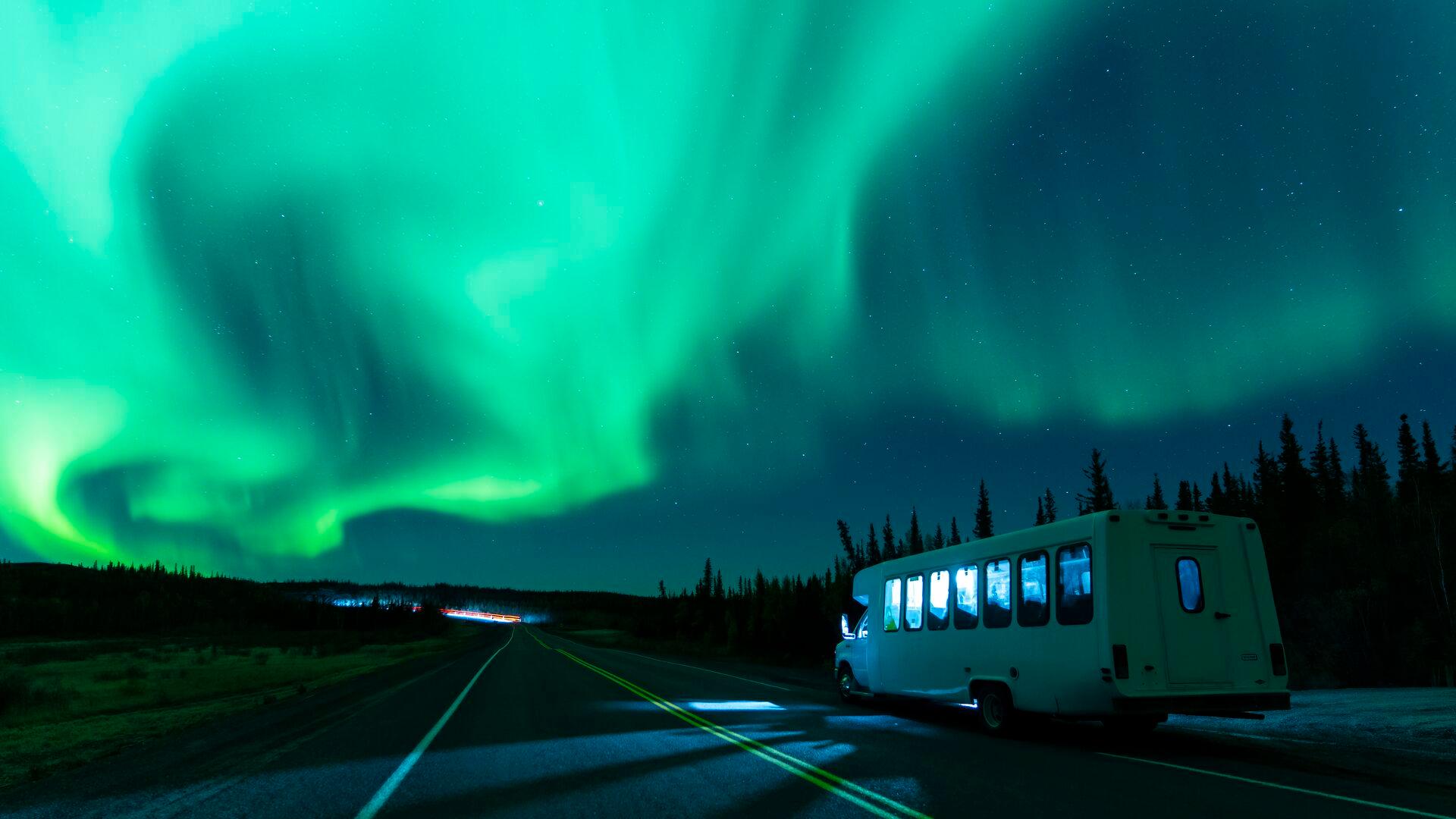 northern lights in the sky with a white bus on road pulled over