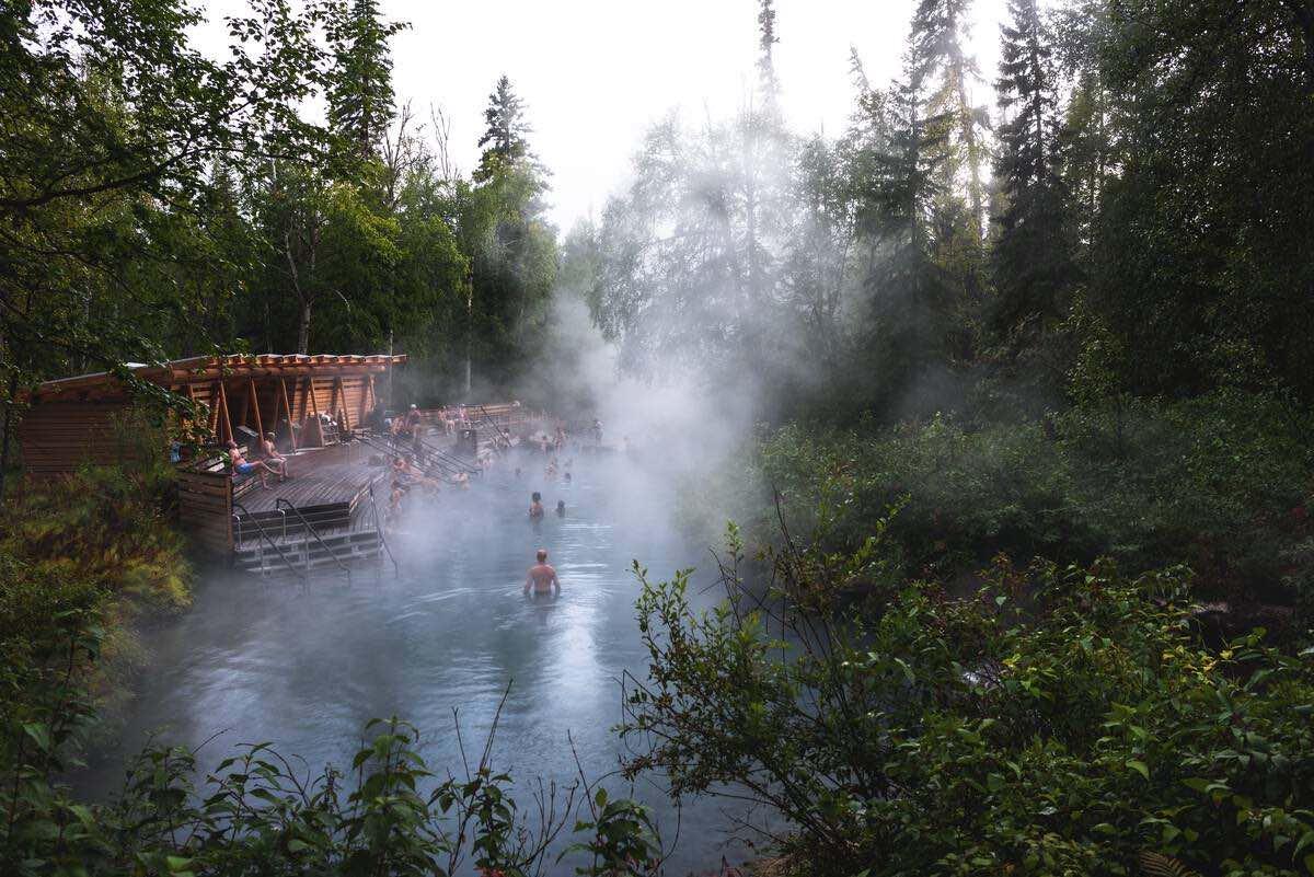 A group of people in the Liard River Hot Springs with steam rising.