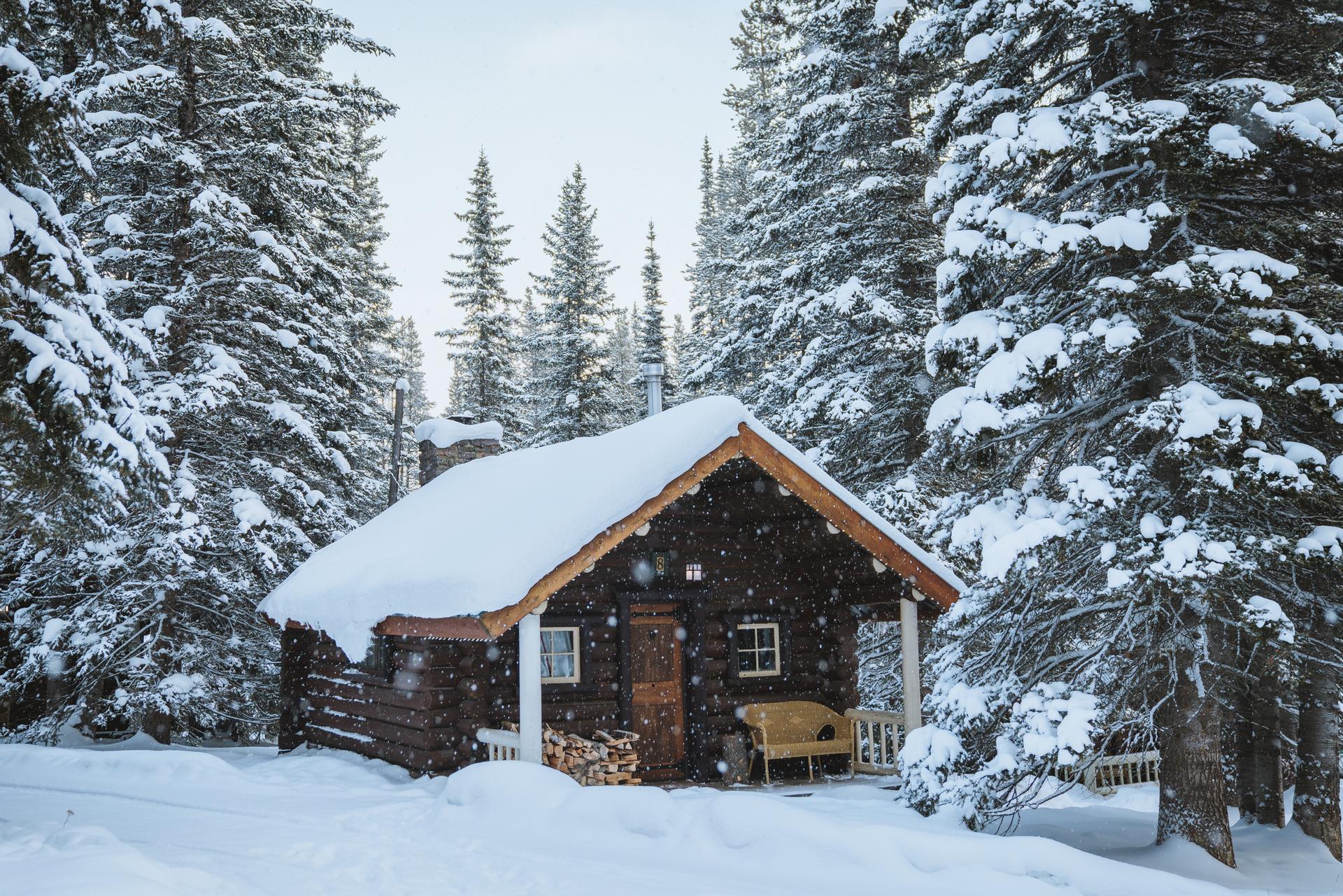 A snow-covered log cabin in a snowy forest scene.