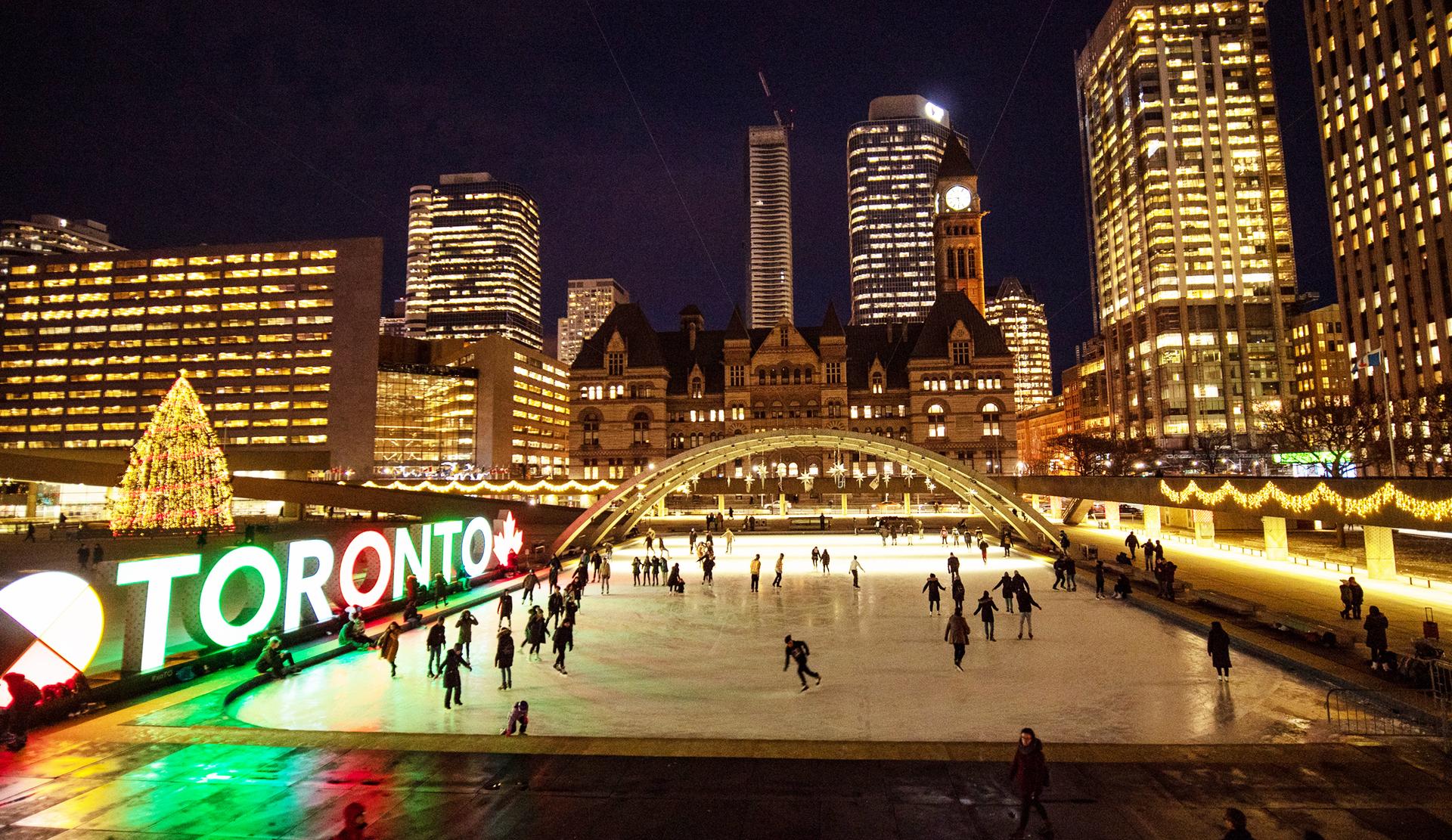 People skating at the Nathan Phillips Square ice rink in downtown Toronto at night.