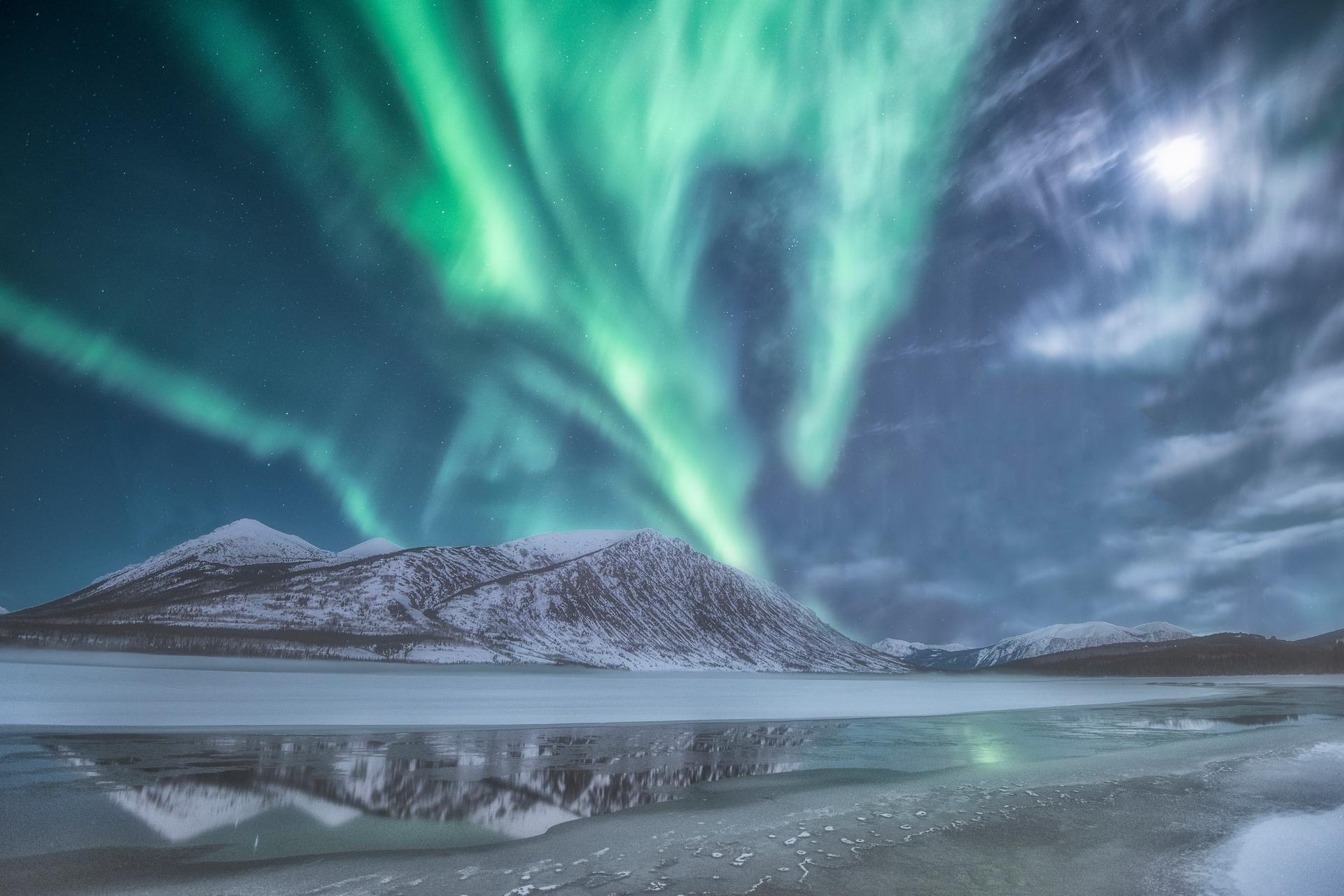 The northern lights above a wintry lake with snowy mountains in the background.