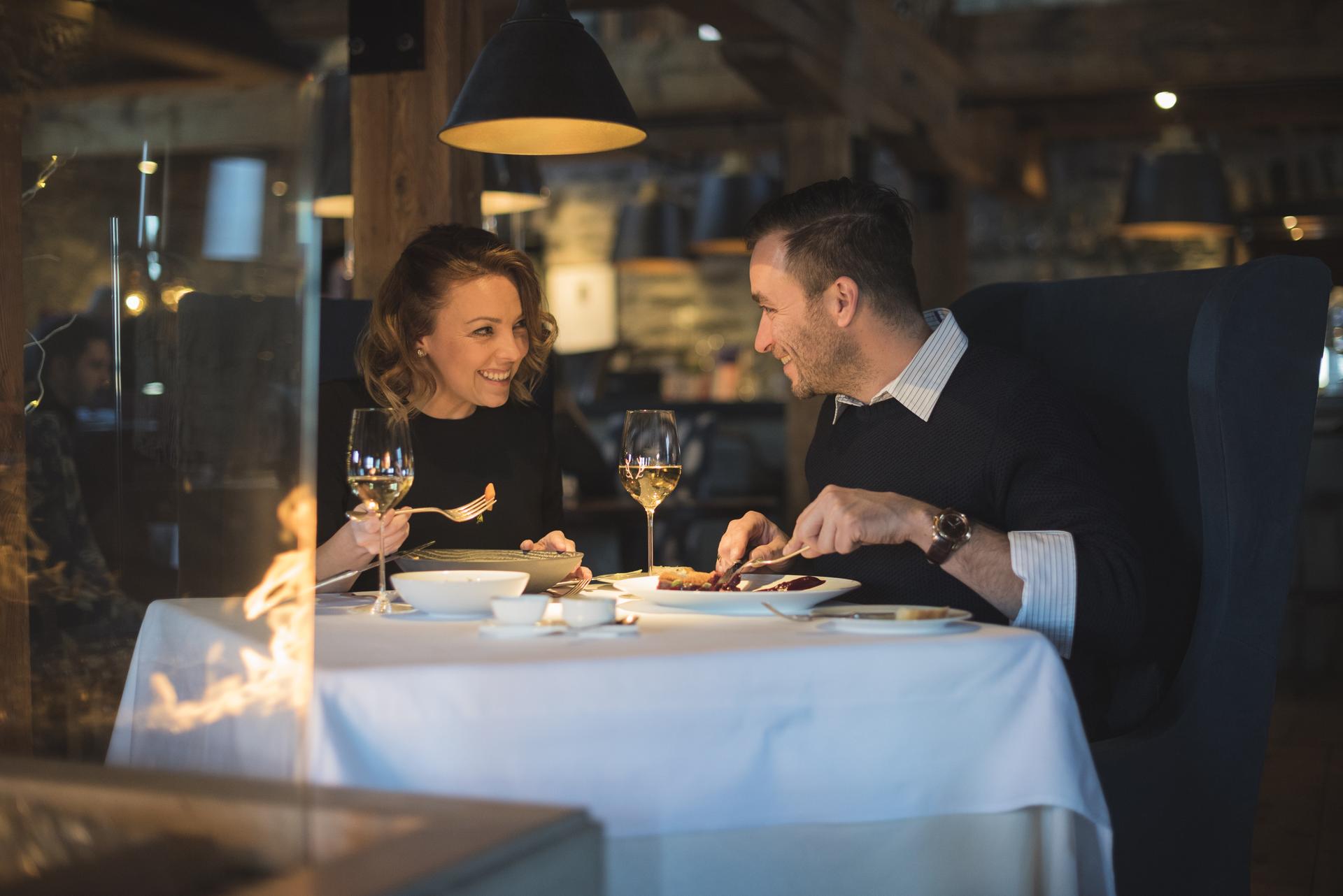 Two people seated at a table in a restaurant with a white table cloth, enjoying their meal.