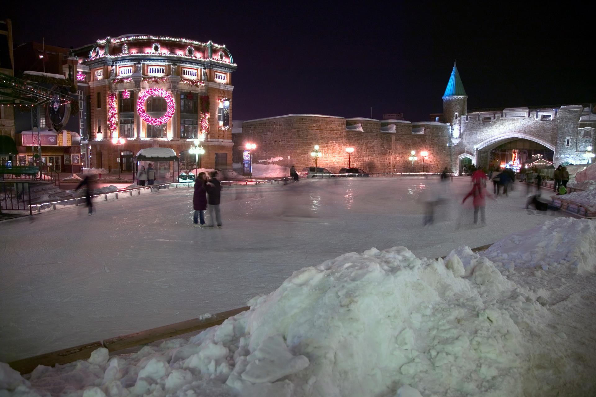 People skating on an outdoor rink at night with Old Quebec fortifications in the background.