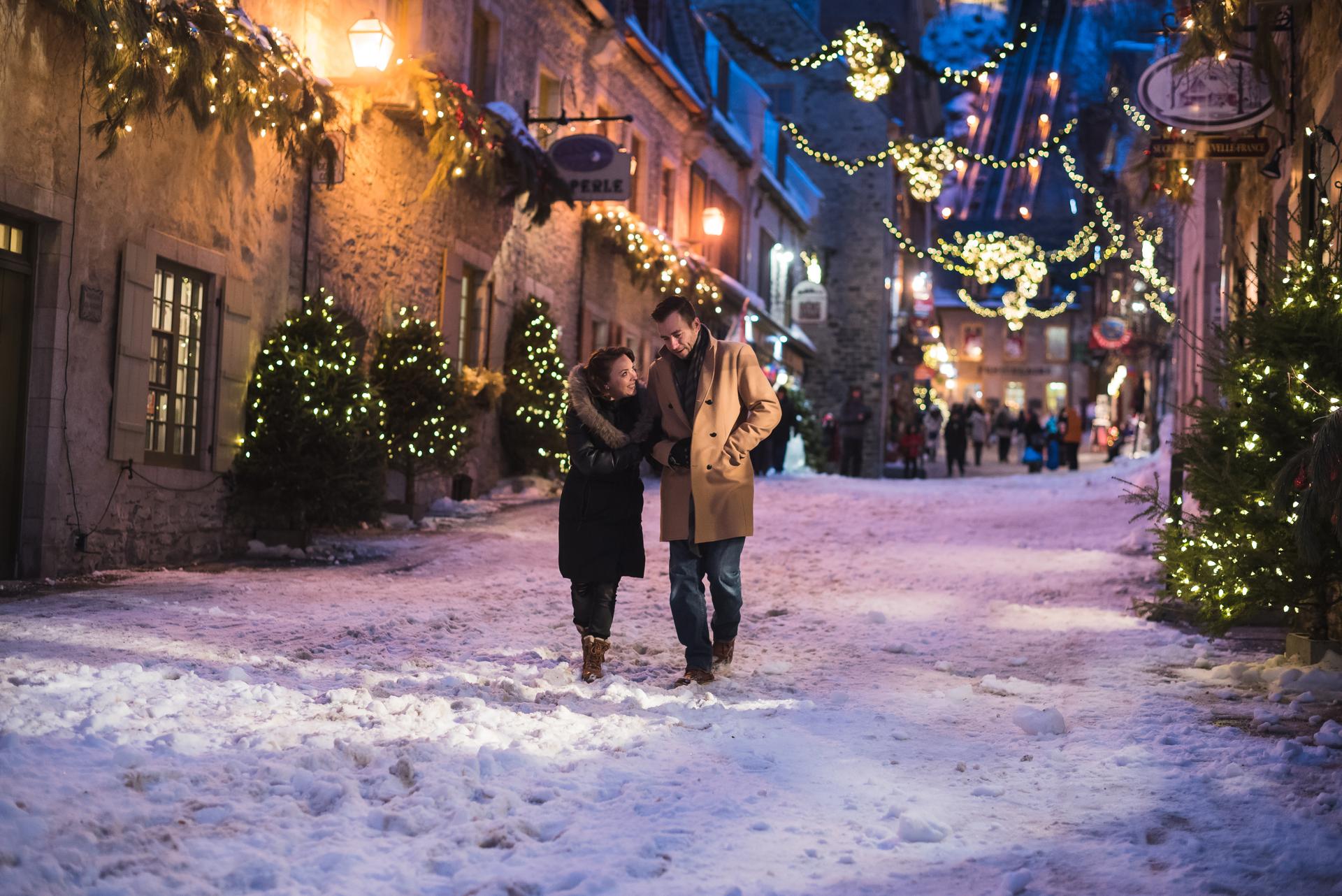 A couple walking down the snowy streets of Old Quebec at night.