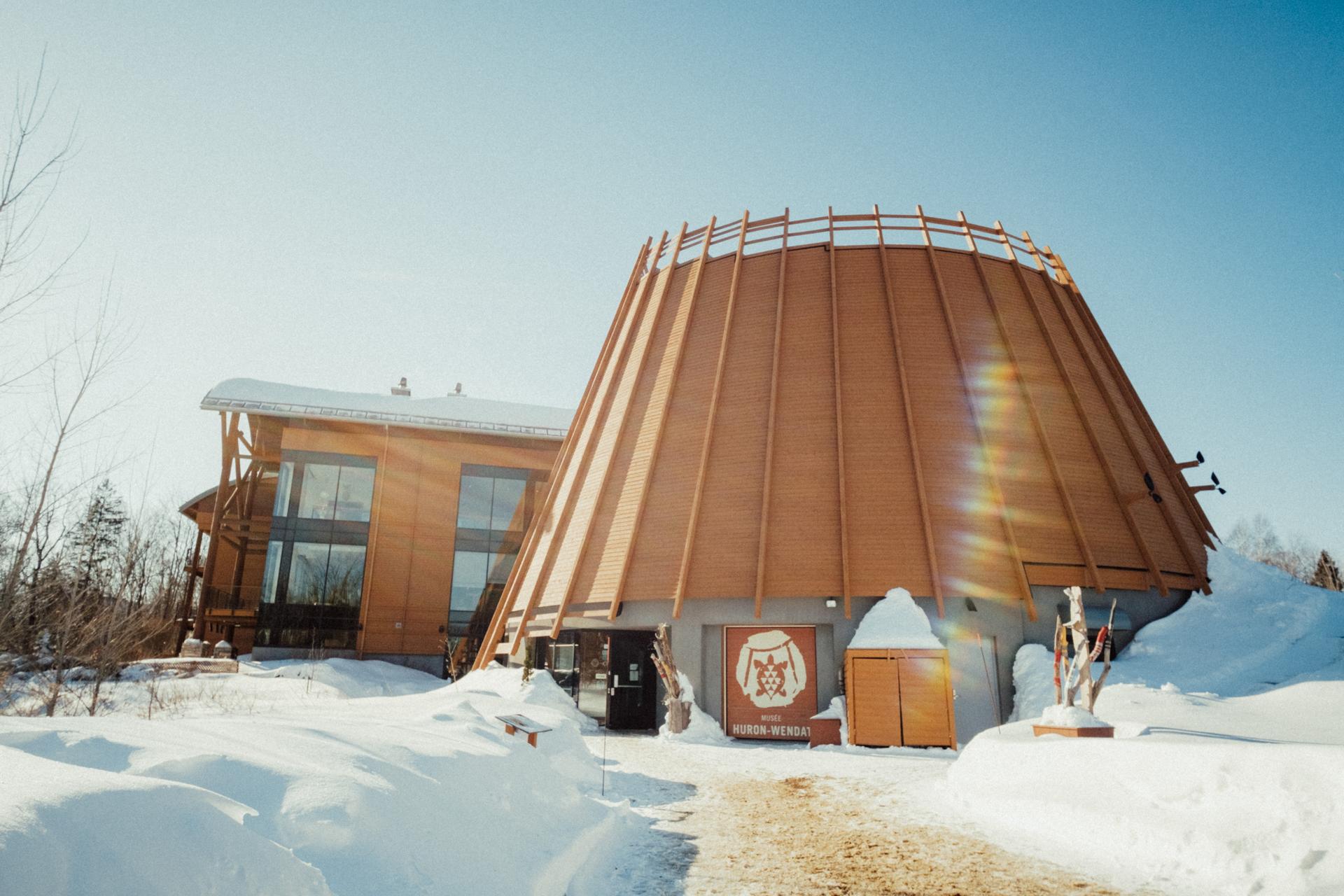 Large wooden conical building in the snow,"Musée Huron-Wendat"