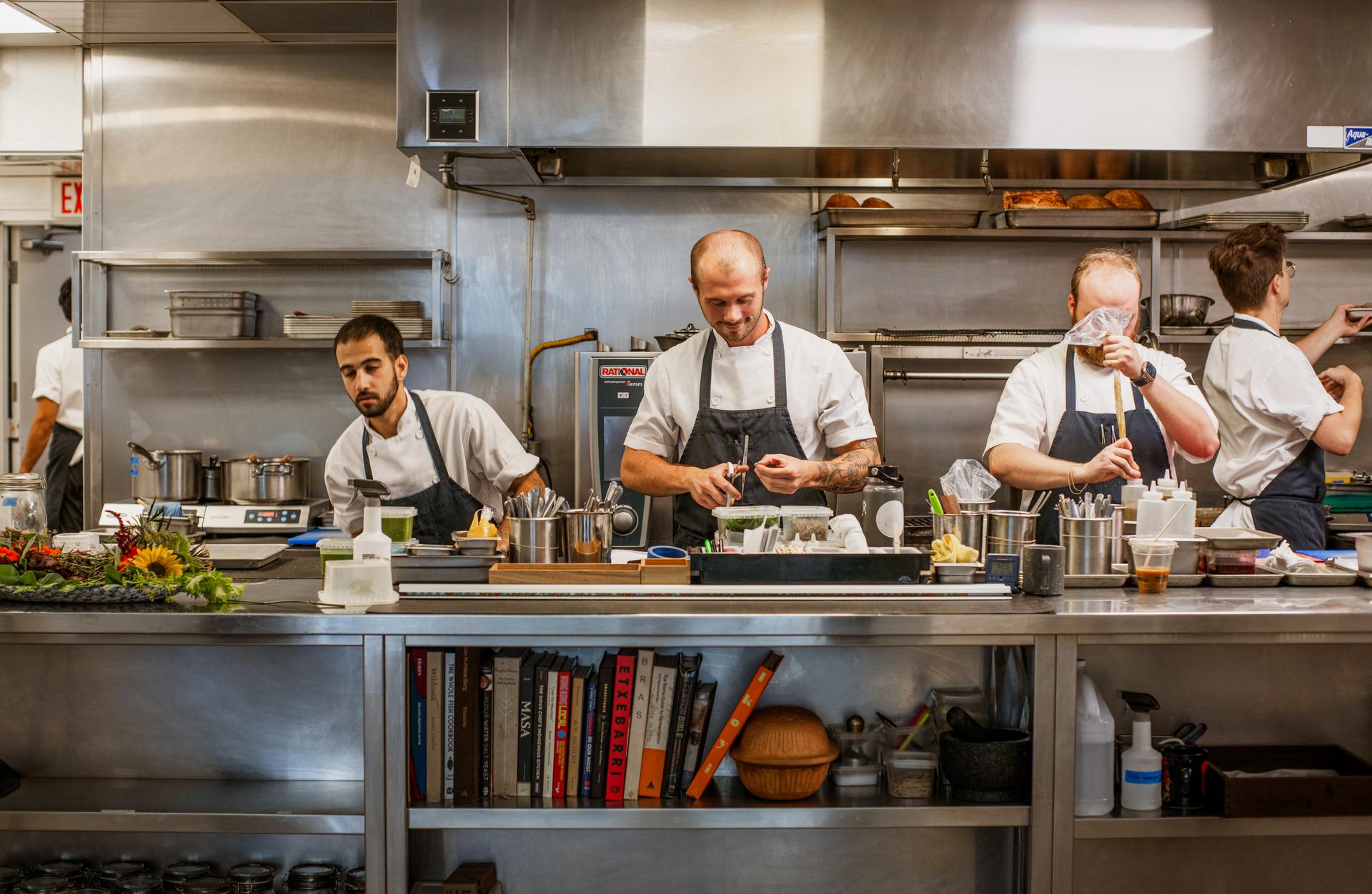 Three chefs preparing food behind a counter in an industrial kitchen.