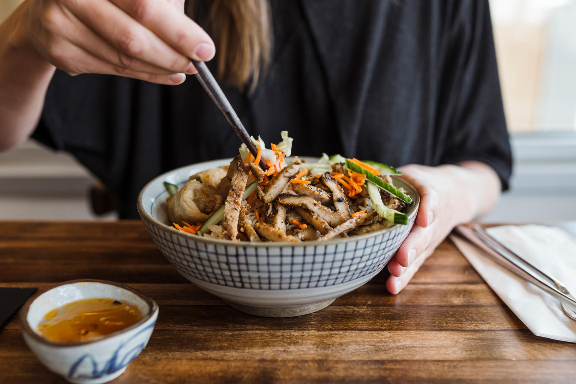 A person using chopsticks to eat a bowl of food at Odd Couple Restaurant in Saskatoon, Saskatchewan