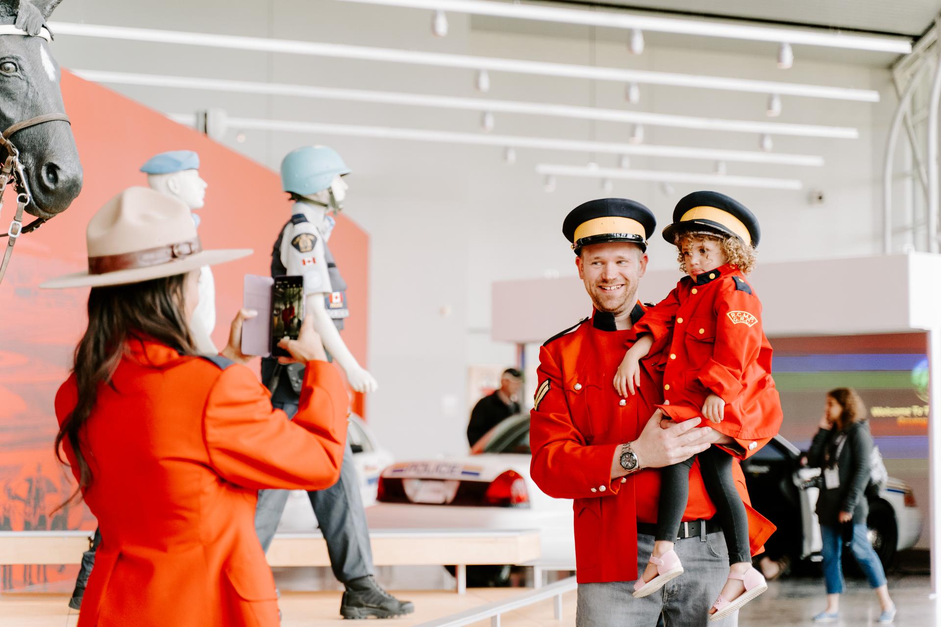 A man and child dressed in RCMP jackets and hats, posing for a photo at the RCMP Heritage Centre.