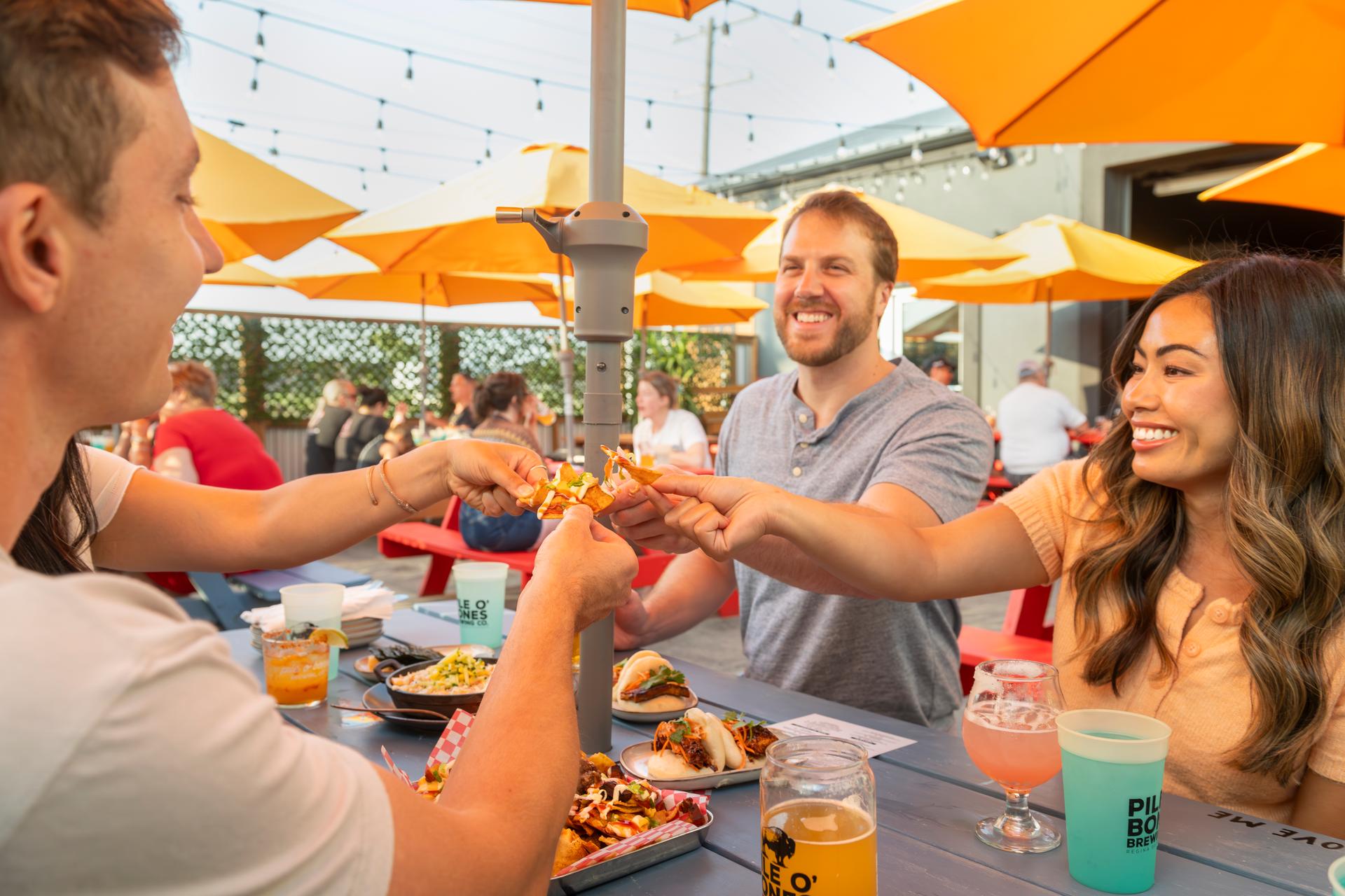 A group of people sharing food and drink at an outdoor patio at Pile O' Bones Brewing in Saskatoon.