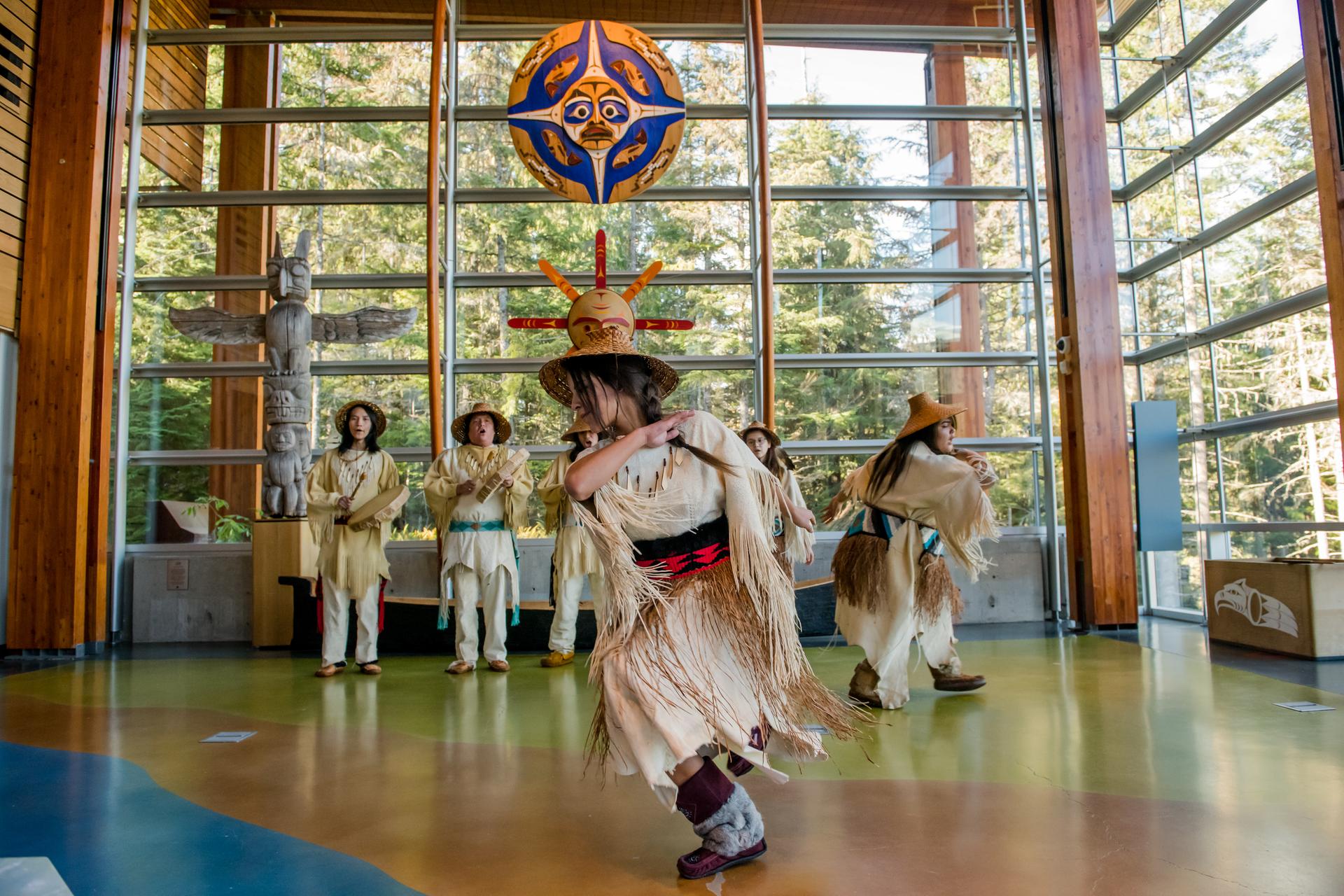 Indigenous dancers in traditional regalia perform inside a cultural center