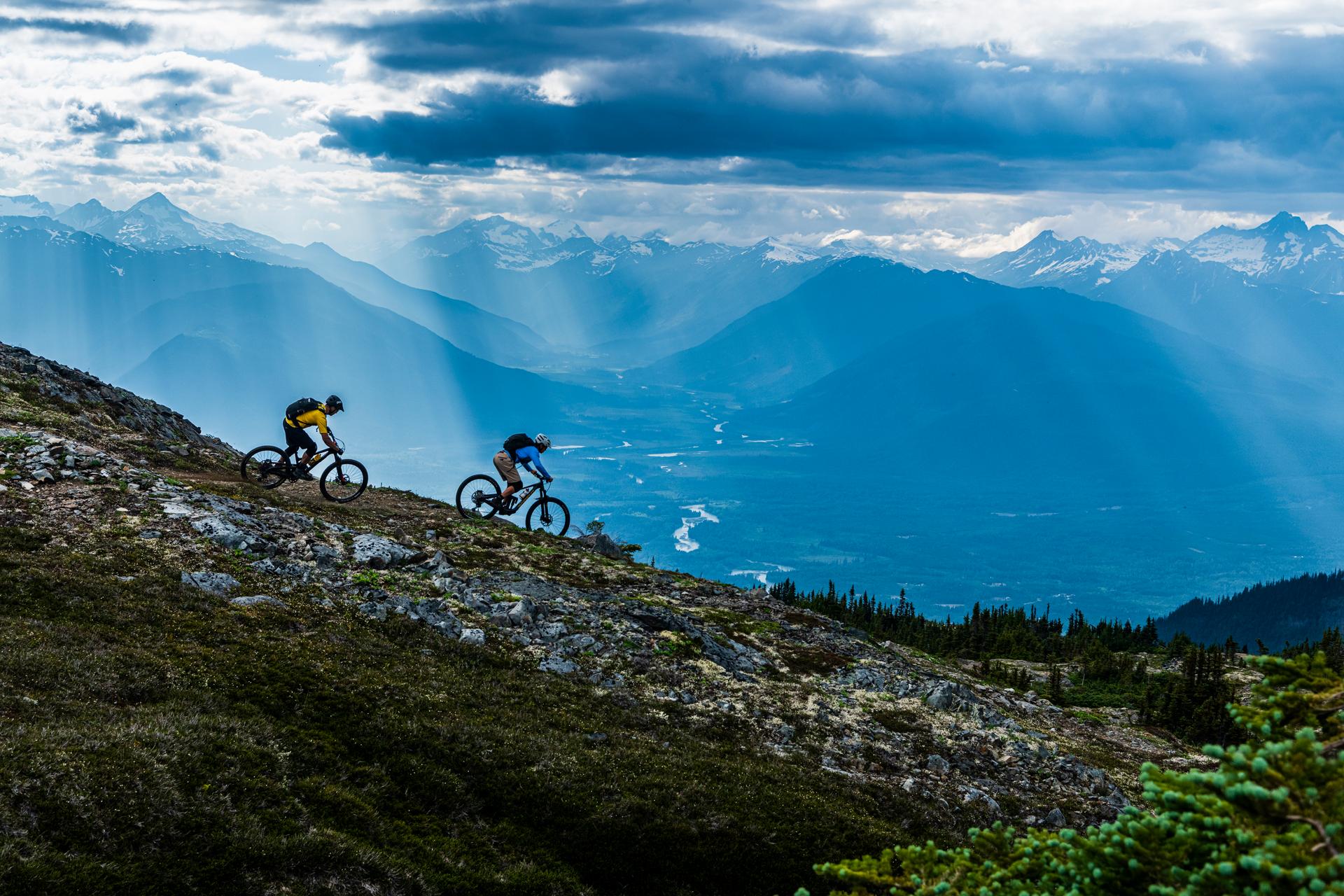 Two mountain bikers riding along a rocky alpine ridge with mountains below