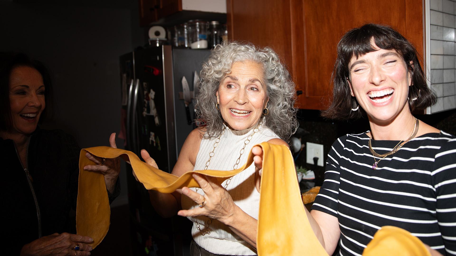 Two people smiling while holding fresh pasta dough in a kitchen