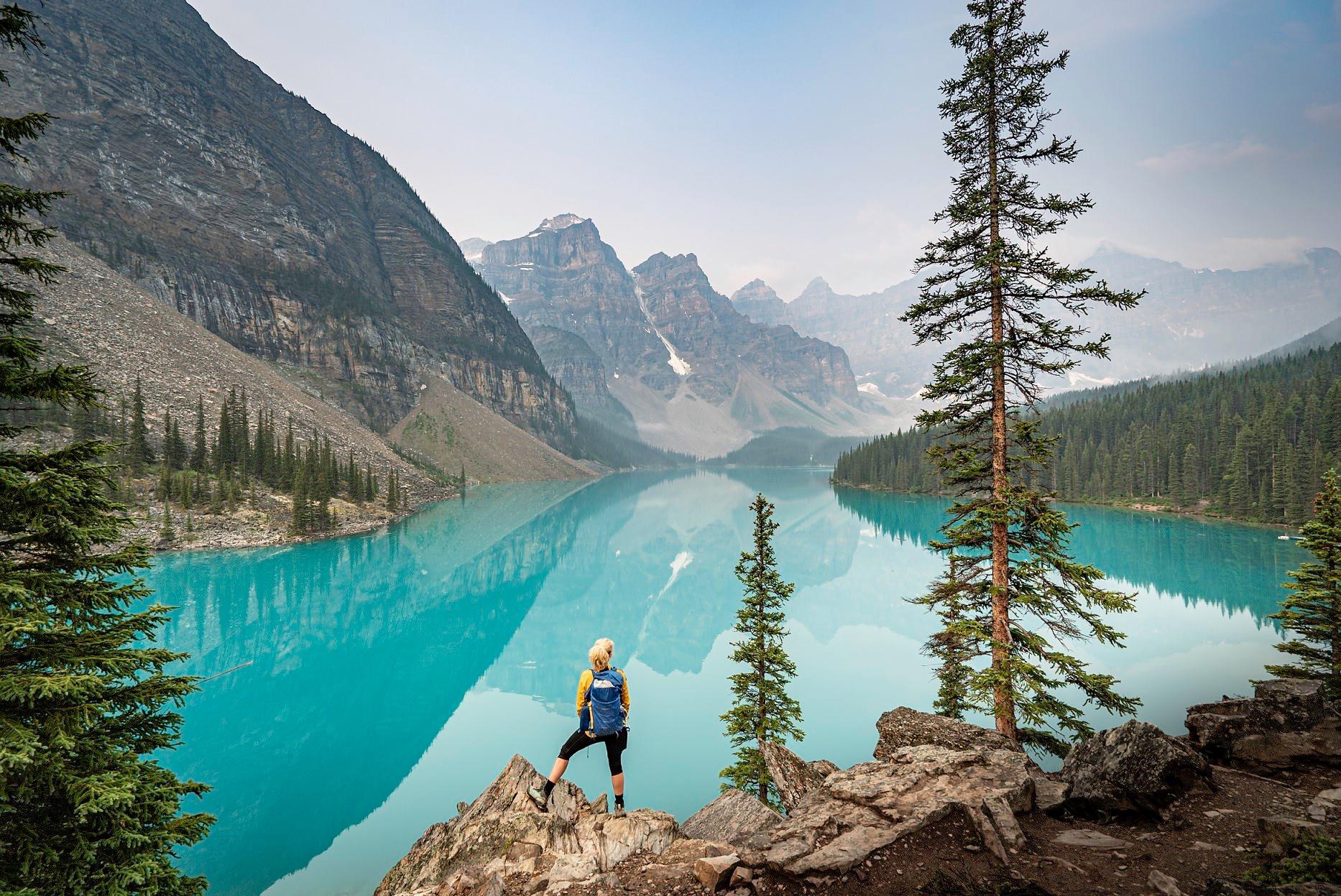 Hiker standing on a rocky overlook above a turquoise mountain lake