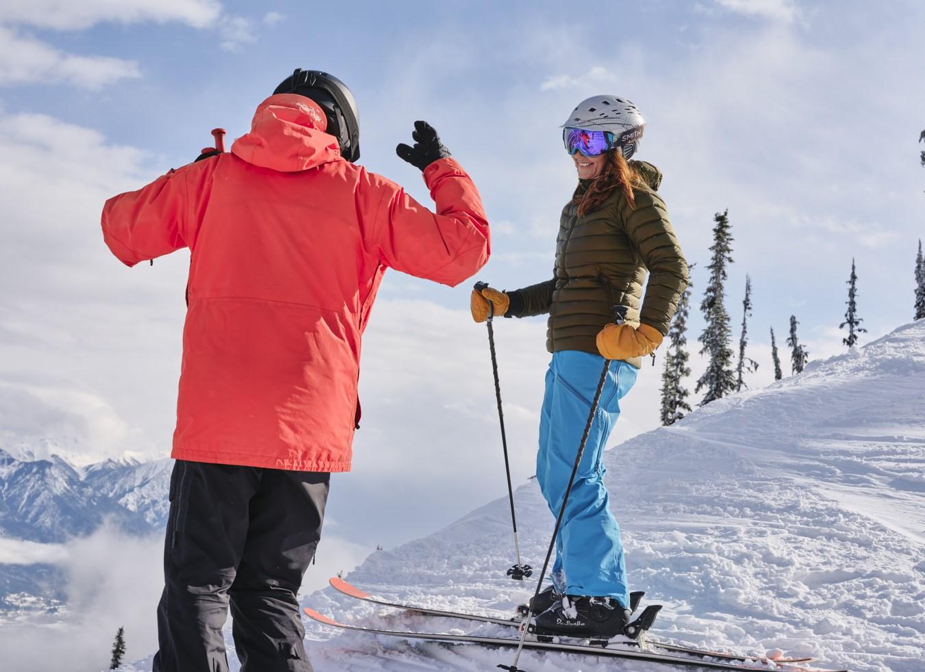 Two skiers high-fiving on a snowy mountain peak