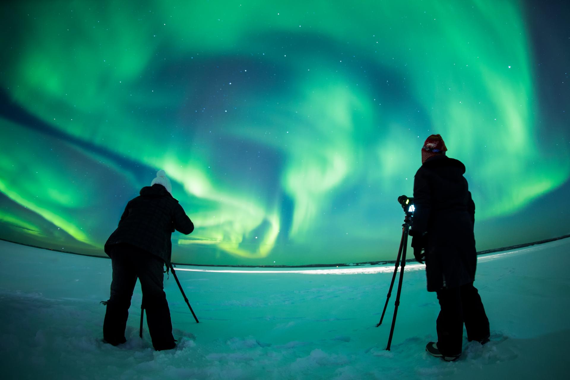 Two photographers capturing vivid northern lights over a snowy landscape