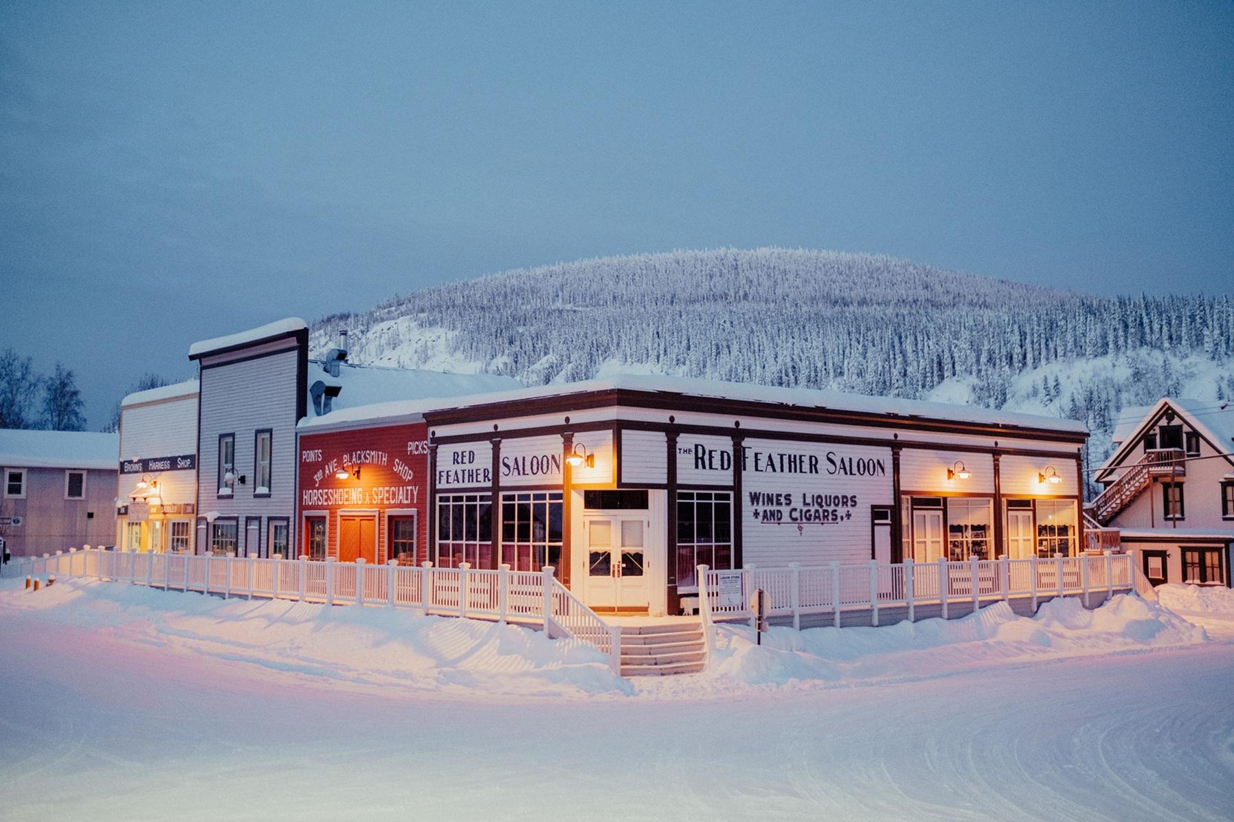 Snow-covered Red Feather Saloon in a northern town, backed by forested hills