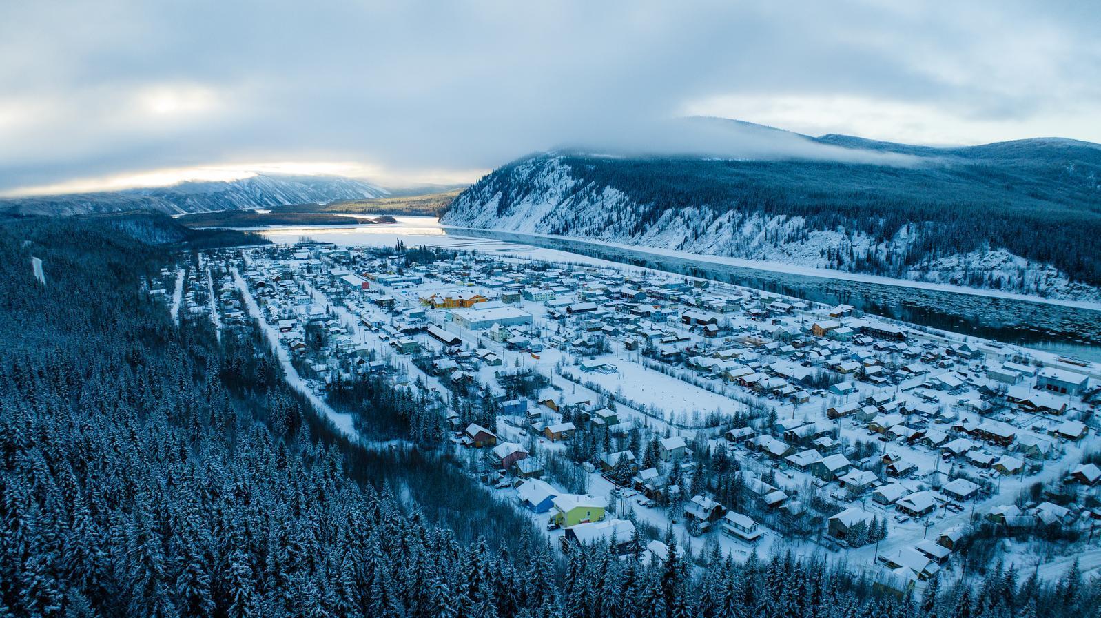 Snow-covered Dawson City along the Yukon River, surrounded by forested hills