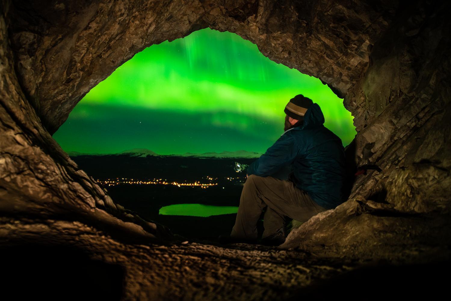 A person watches the northern lights over the city of Whitehorse from a cave.