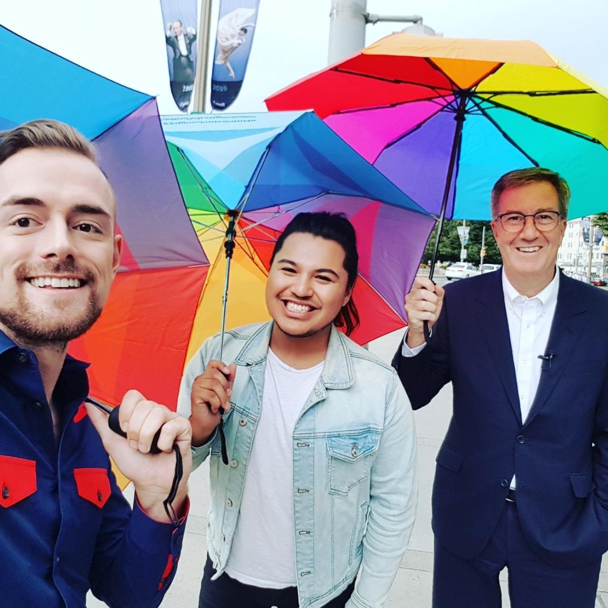 Brett and Cameron hold up rainbow umbrellas