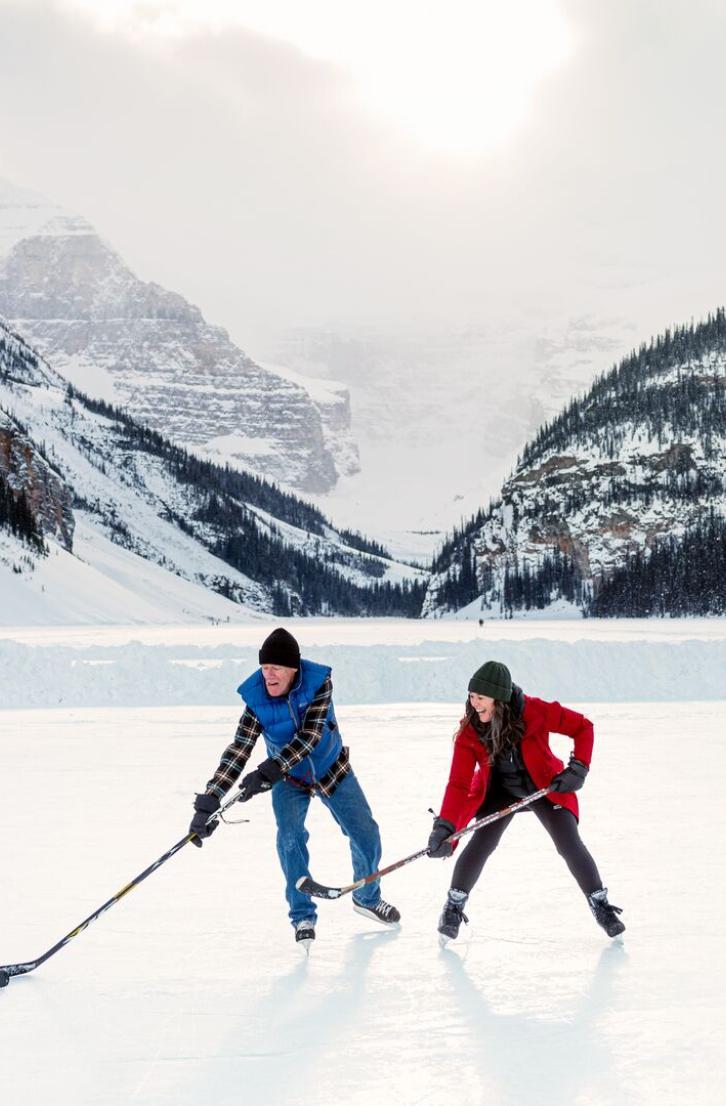 Two people playing ice hockey in front of large mountains.