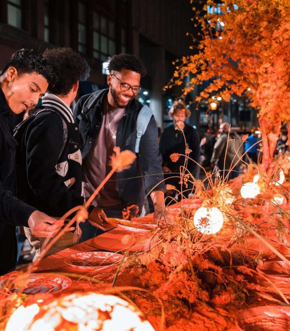 A group of people enjoy a festive outdoor dining experience with autumn-themed floral arrangements.