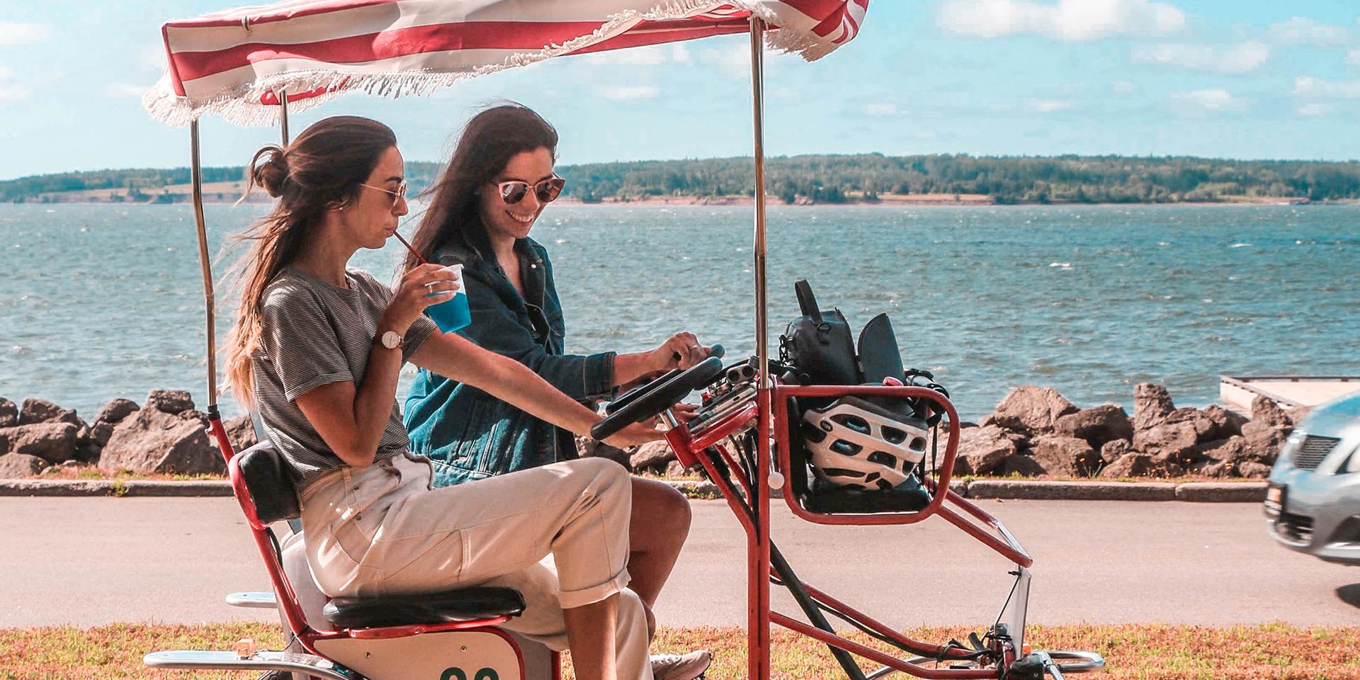 Two travelers ride a tandem bicycle cart through Victoria Park in Charlottetown, by the ocean