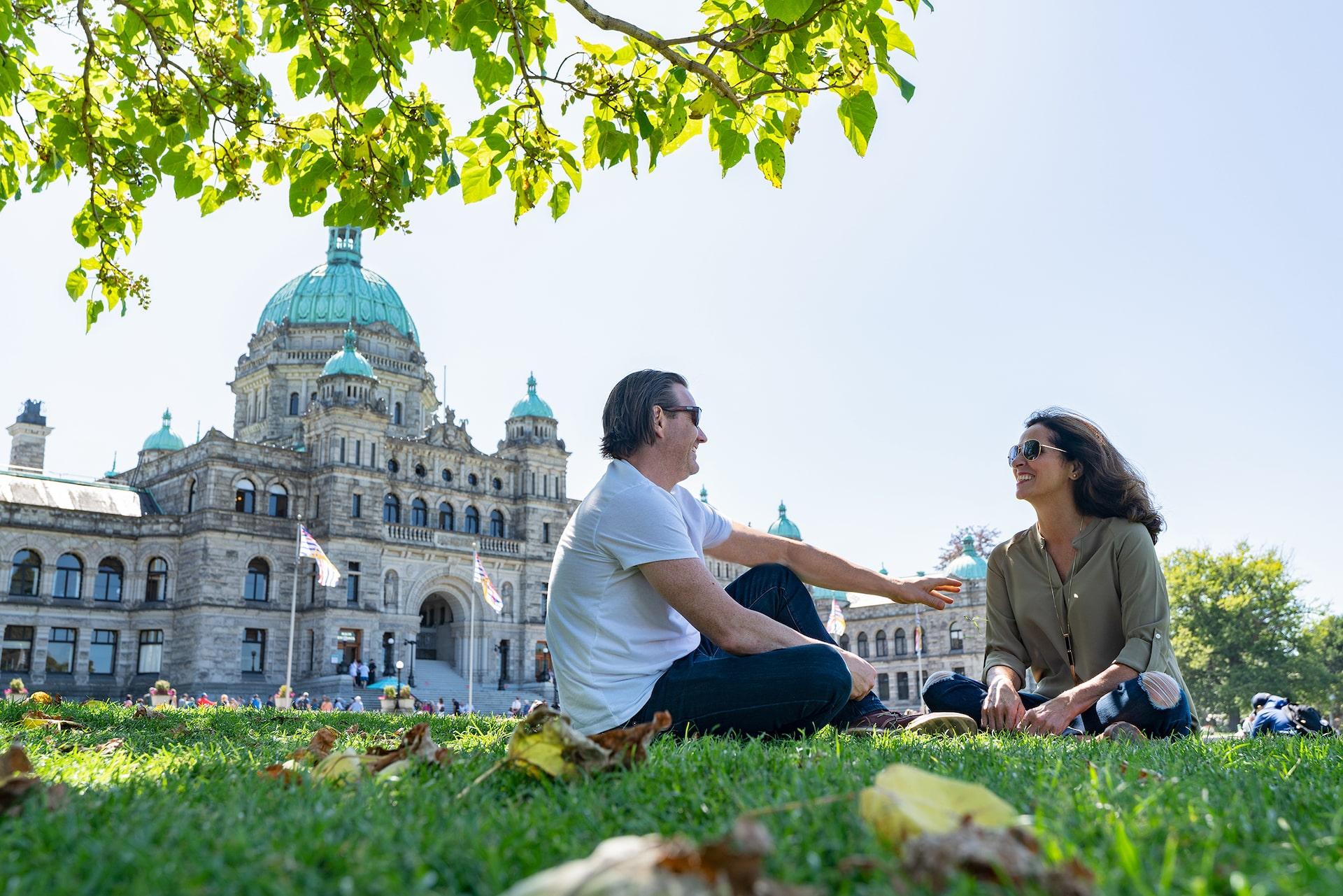 A couple sitting on the lawn outside BC Legislature in Victoria, BC