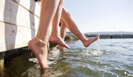Two pairs of feet dangling off the dock into the water