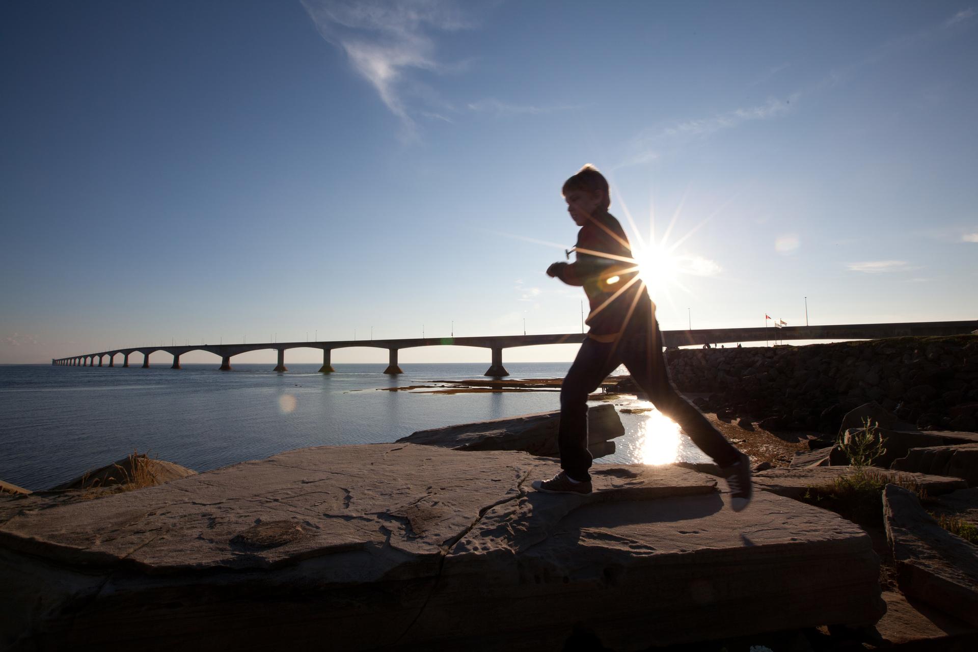 A young kid runs on the rocks under the Confederation Bridge in Prince Edward Island