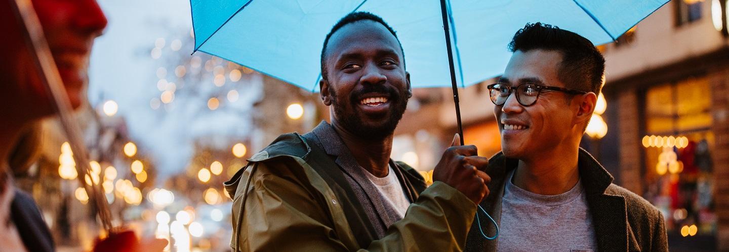 Two men share a blue umbrella