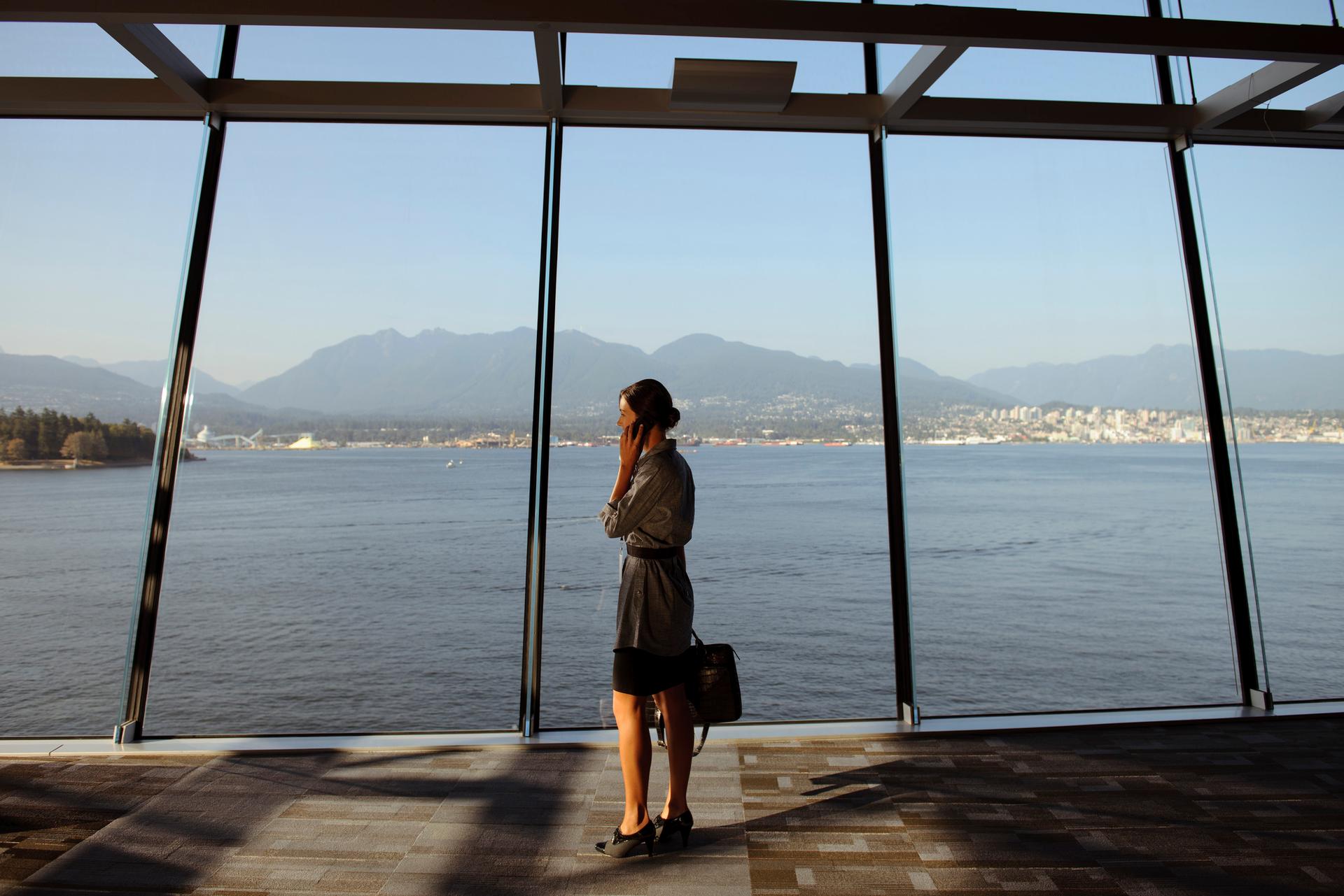 A woman stands next to a large window looking out on Vancouver's harbour