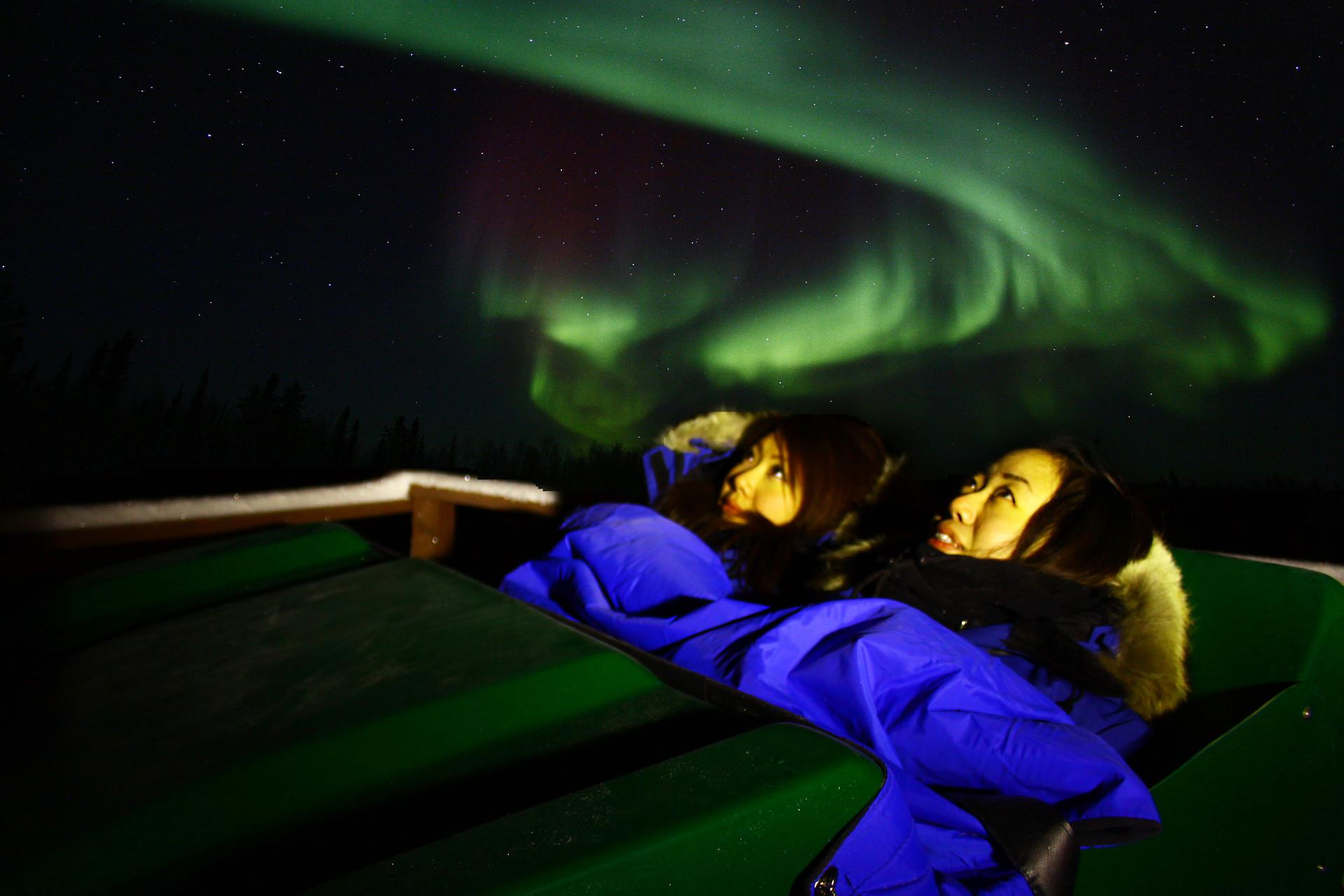 Two people lying under sleeping bags watching the northern lights in Yellowknife, Northwest Territories