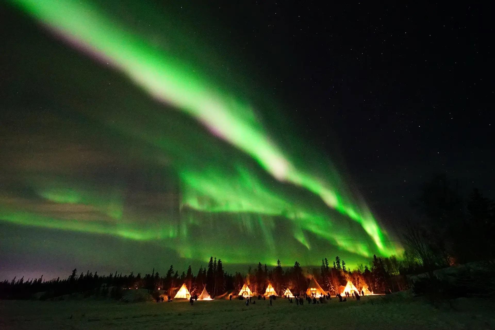 Aurora Village, teepees under vibrant green northern lights, Northwest Territories, Canada