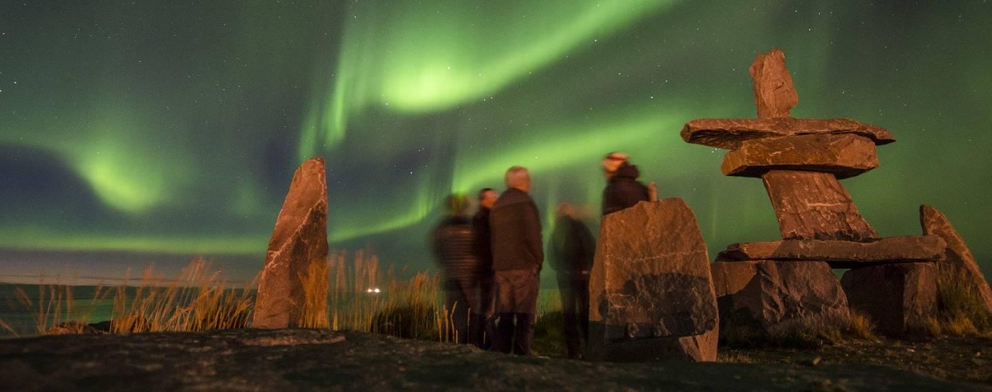 People gathered under the northern lights, next to an Inukshuk