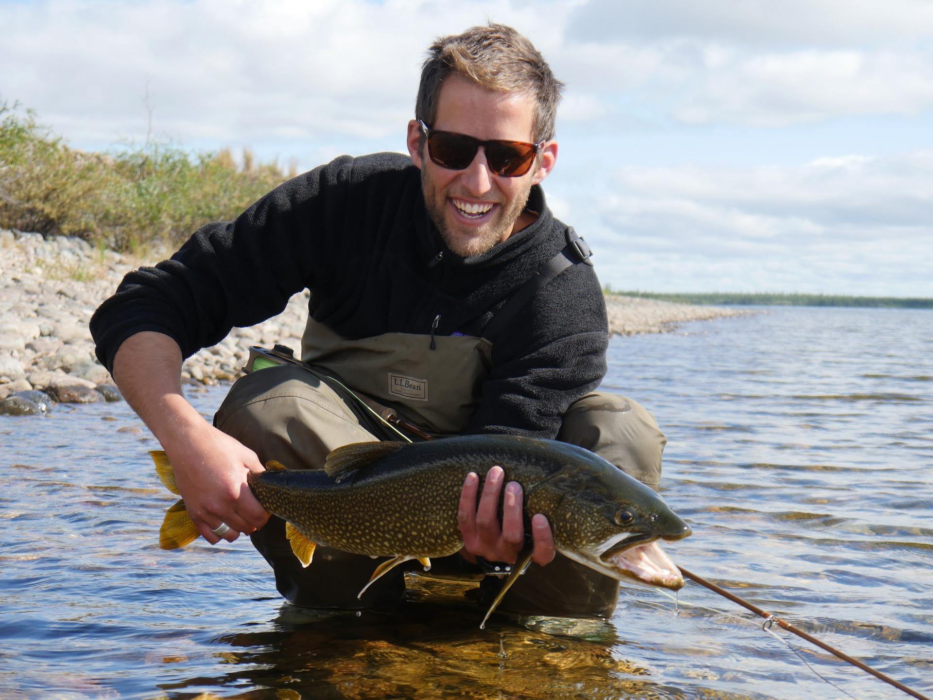 A man holds a fish he has caught in a river