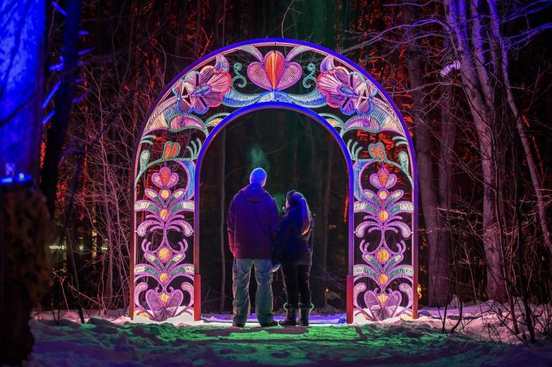 A couple stands under an illuminated arch in winter