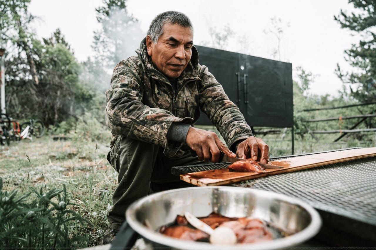 Person wearing camo, cooking salmon jerky in a forested area