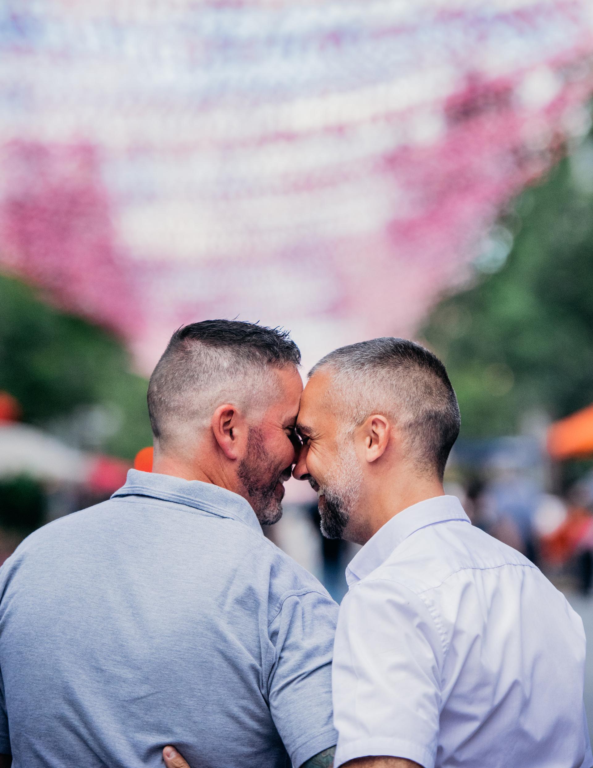 Two men putting their heads together as they walk down a street with pink balls strung overhead.