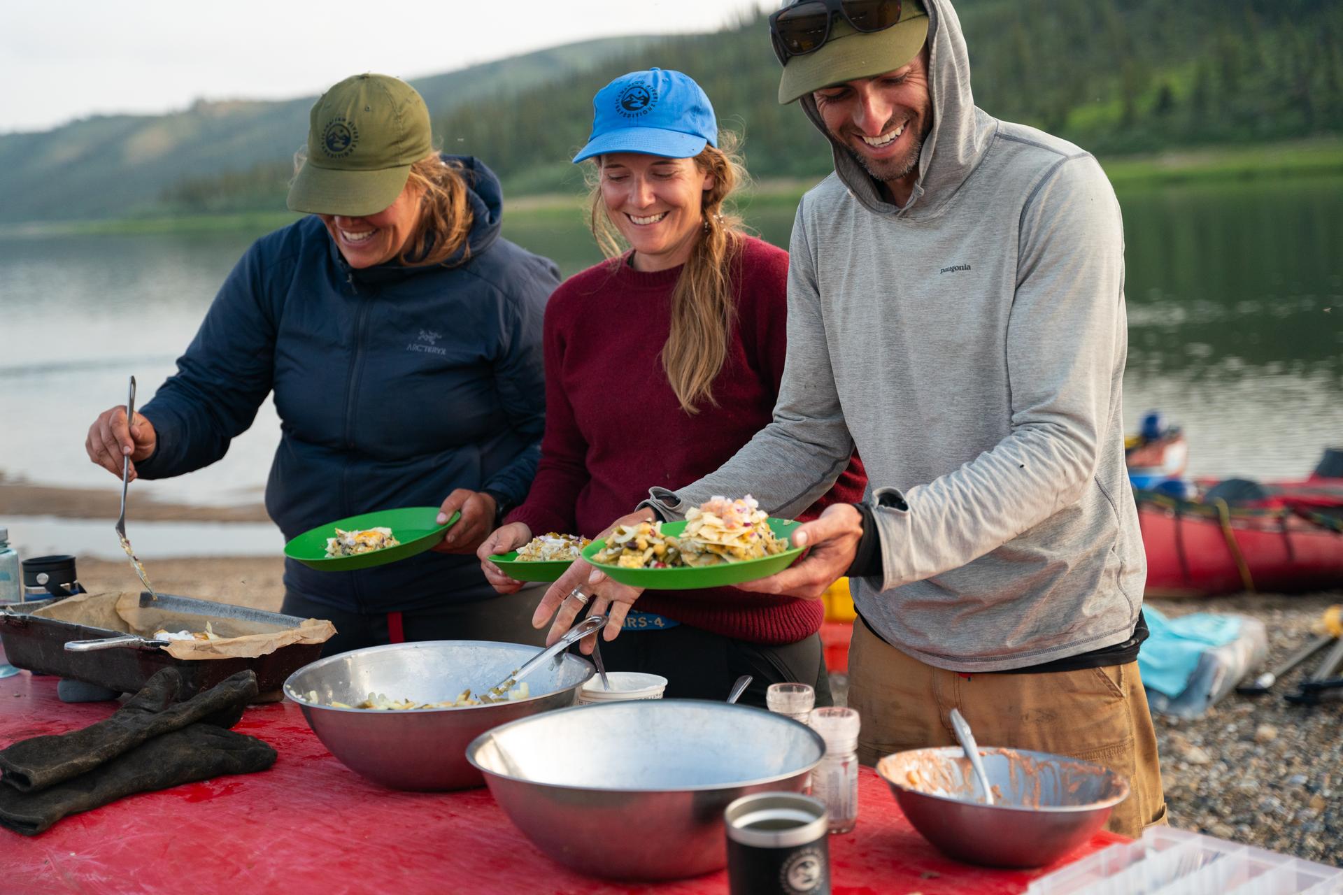 Three people plating salads outside by a lake